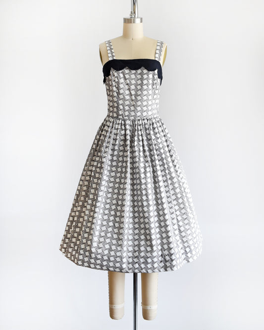 A vintage 1950s white dress with a  black fern motif that forms a diamond print. The dress has a black scalloped neckline and fit and flare skirt.