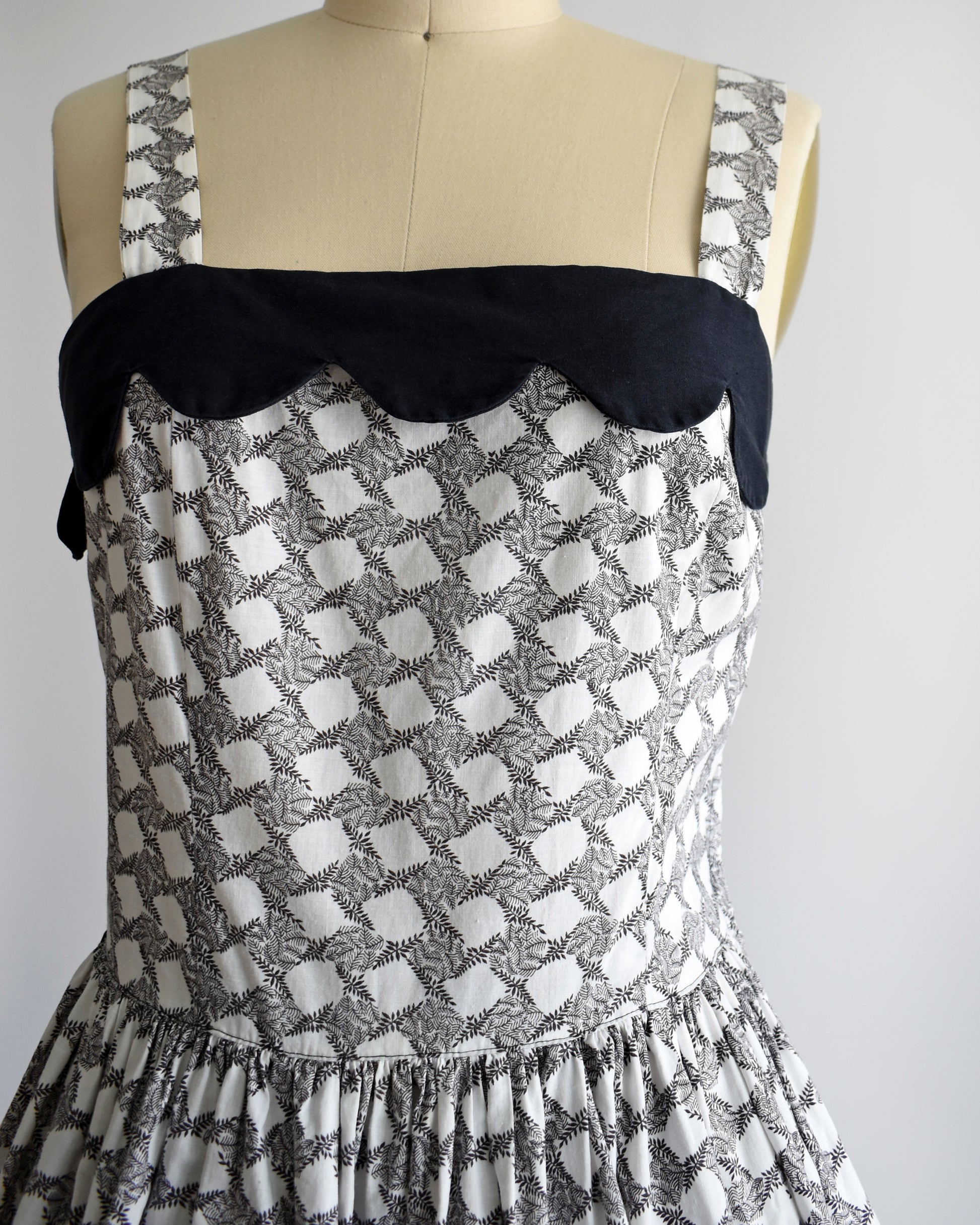 Close up of the bodice which features a black scalloped neckline and black fern print.