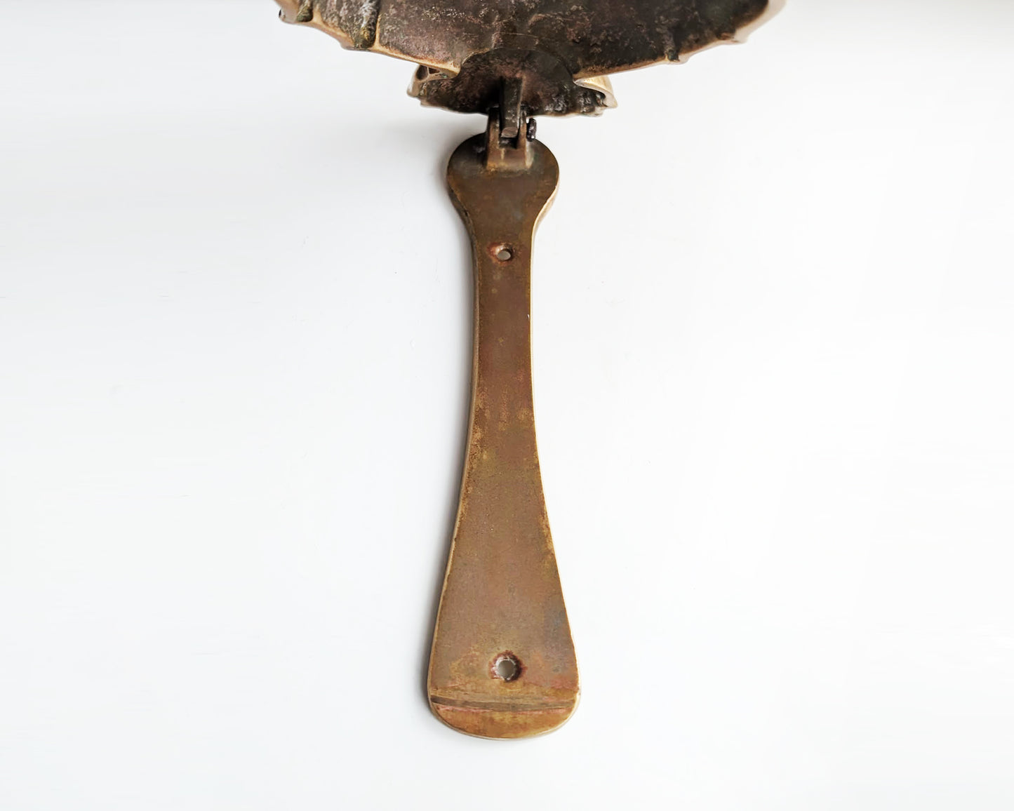 the underside view of the brass strip on a vintage brass pineapple door knocker