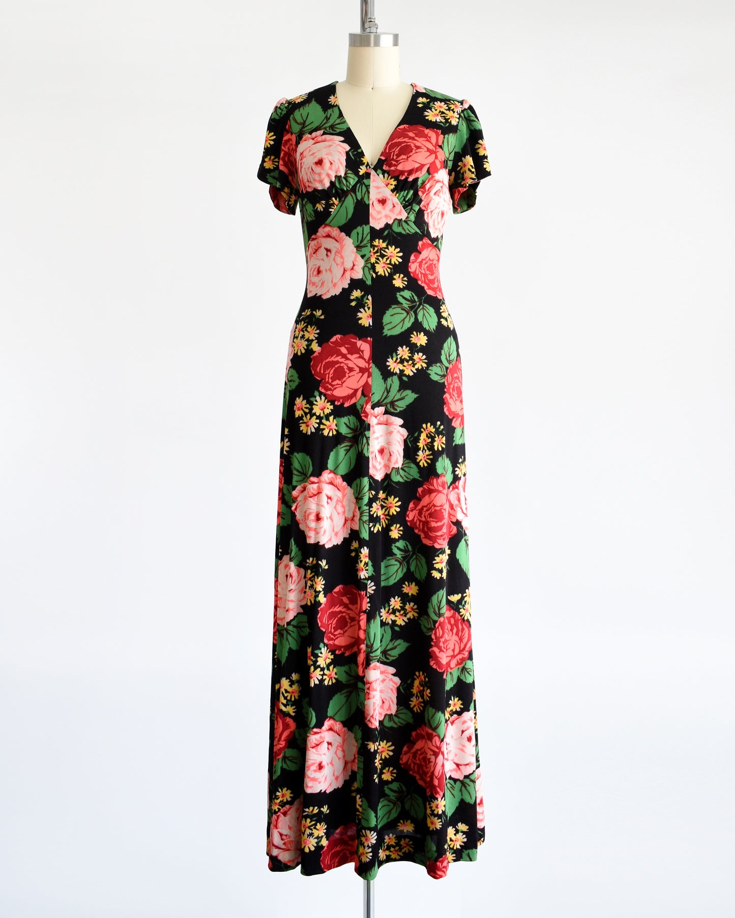 A vintage 1970s black floral maxi dress features a vibrant floral pattern of red and pink roses, green leaves, and yellow and orange daisies.
