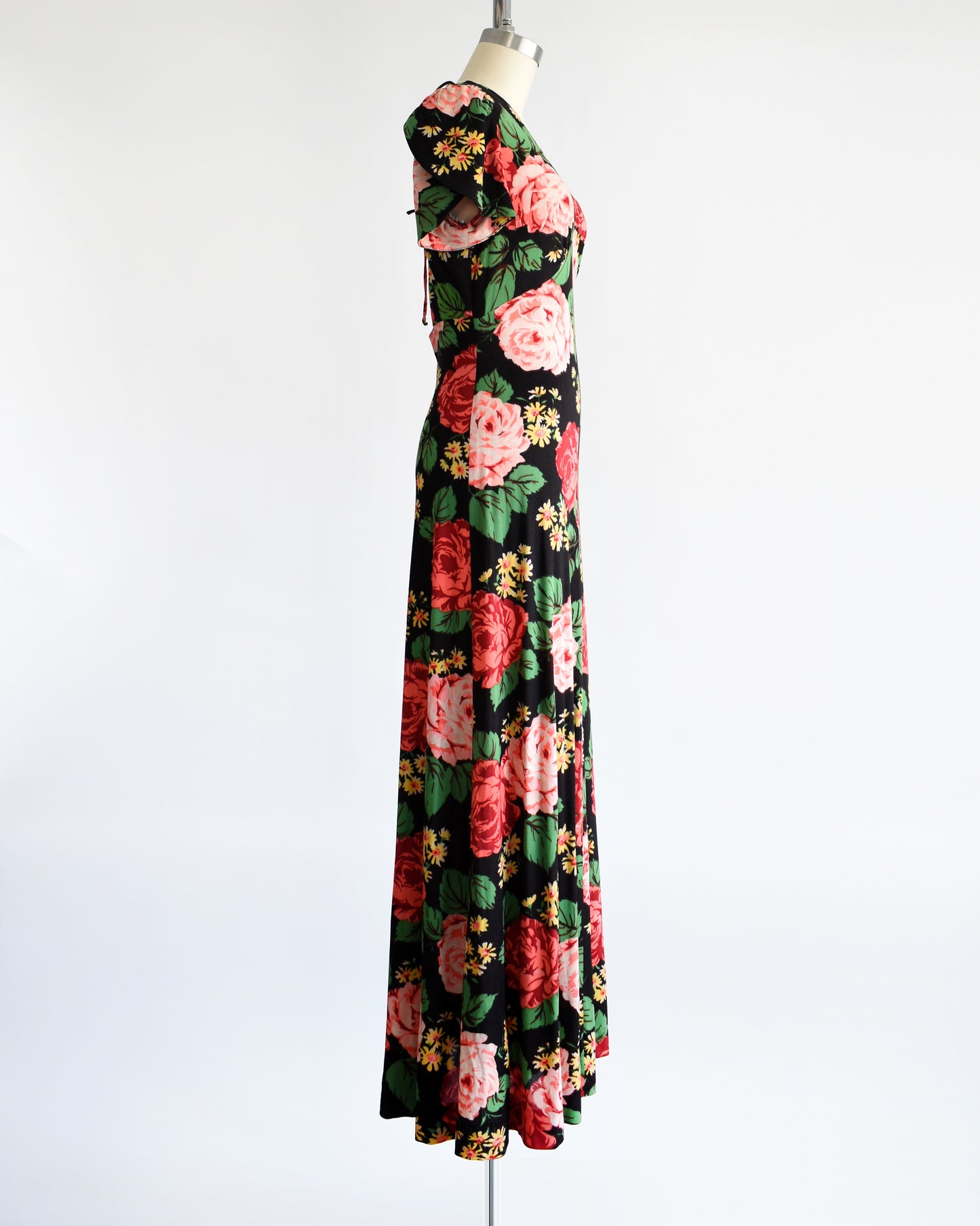 Side view of a vintage 1970s black floral maxi dress features a vibrant floral pattern of red and pink roses, green leaves, and yellow and orange daisies.