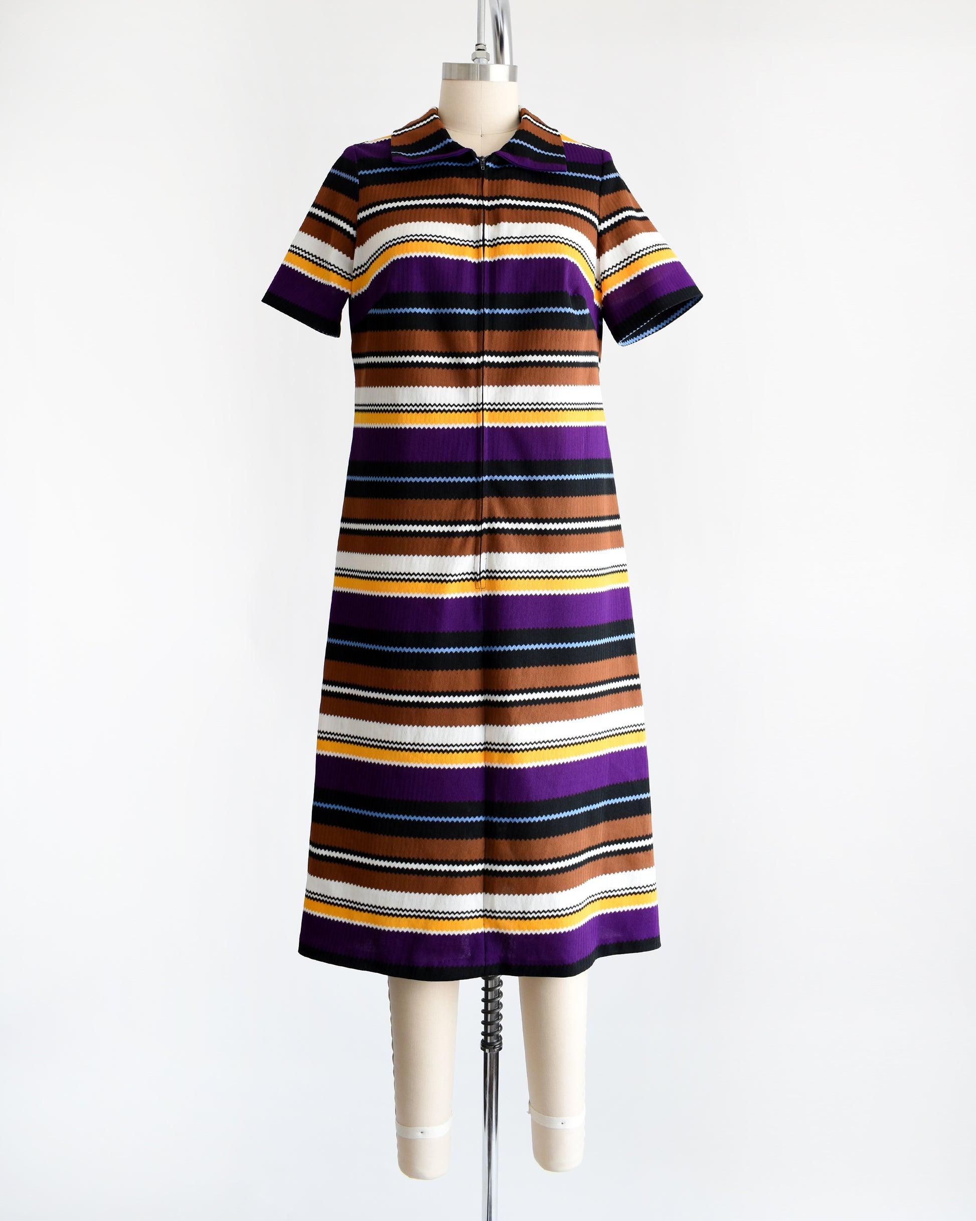 Front view of a vintage 1970s striped mod dress that has black, brown, white, blue, yellow, and purple horizontal stripes with zigzag edges. The dress features a zipper down the front which is zipped up in this photo.