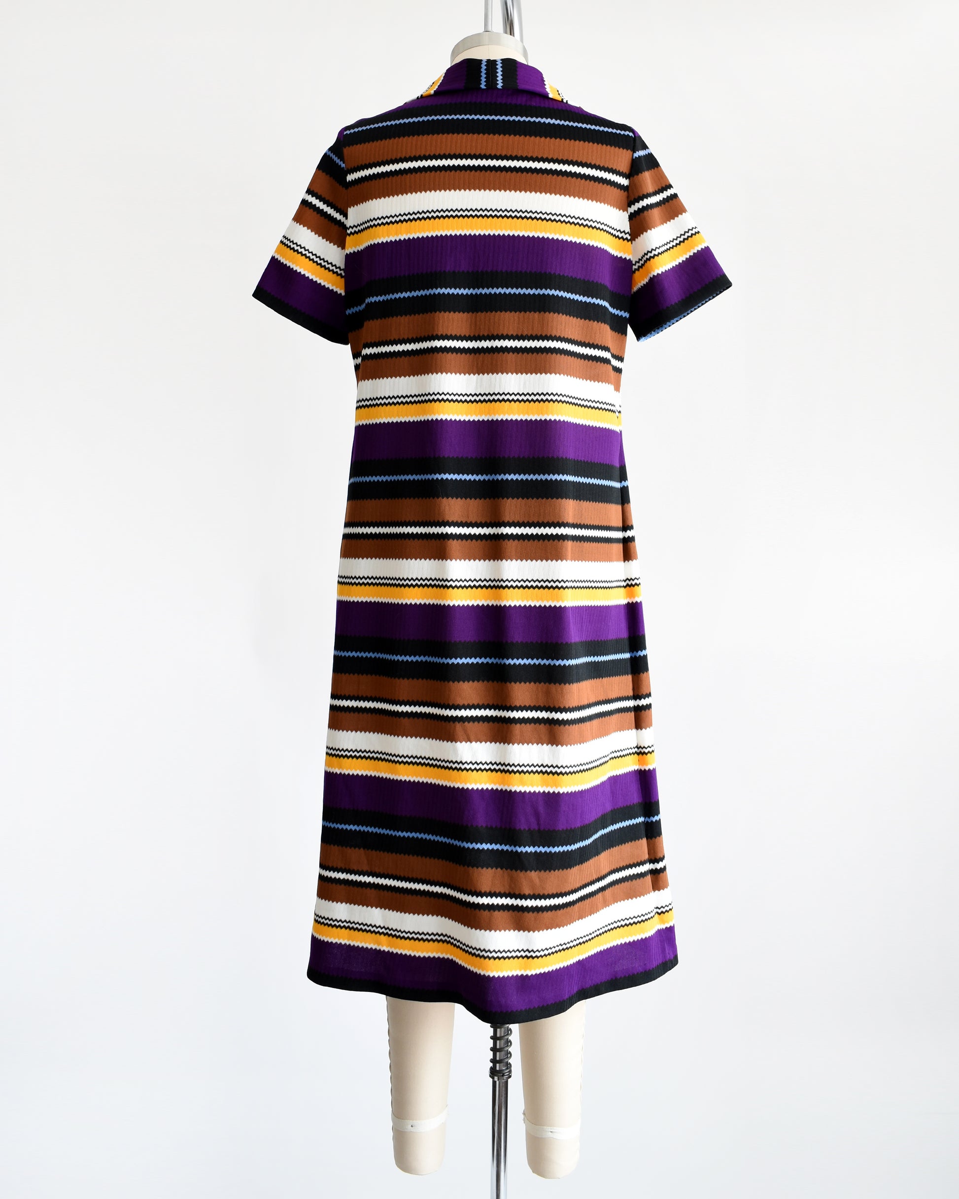 Back view of a vintage 1970s striped mod dress that has black, brown, white, blue, yellow, and purple horizontal stripes with zigzag edges.