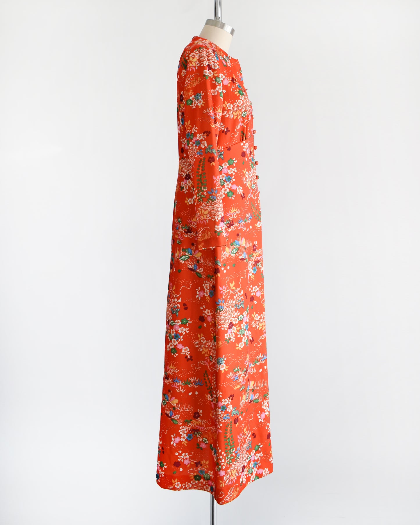 Side view of a vintage 1970s maxi dress features a vibrant red-orange hue, with a delightful floral and dotted print in homage to traditional Japanese flower designs. 