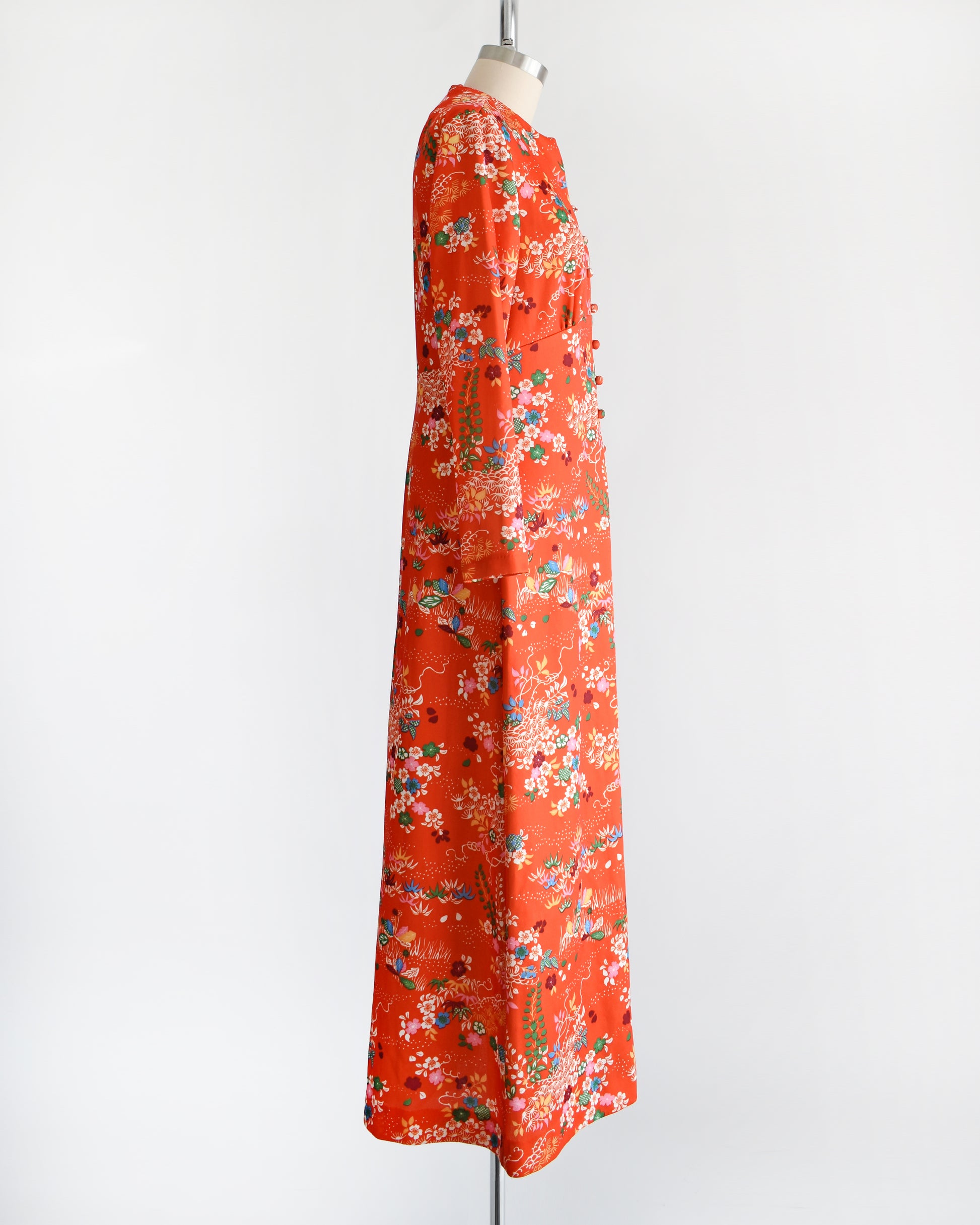 Side view of a vintage 1970s maxi dress features a vibrant red-orange hue, with a delightful floral and dotted print in homage to traditional Japanese flower designs. 
