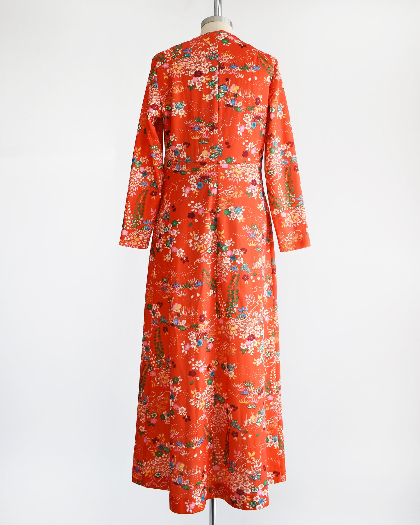 Back view of a vintage 1970s maxi dress features a vibrant red-orange hue, with a delightful floral and dotted print in homage to traditional Japanese flower designs.