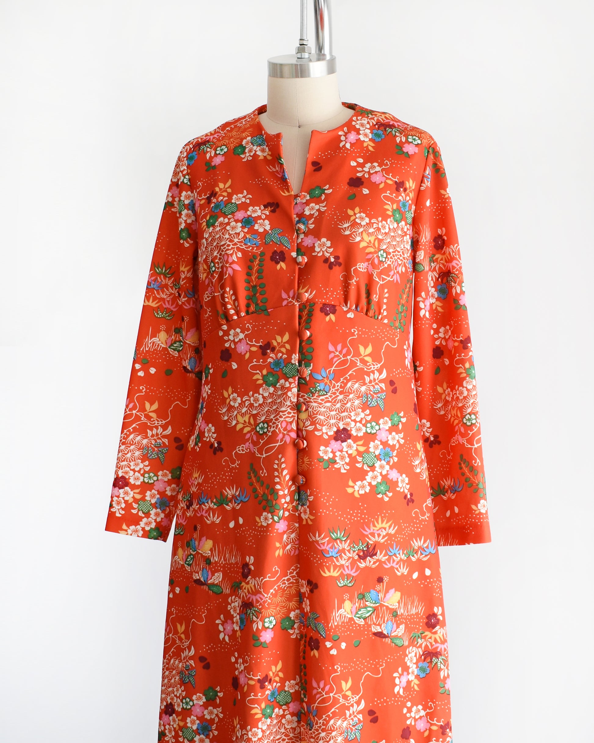 Side front view of a vintage 1970s maxi dress features a vibrant red-orange hue, with a delightful floral and dotted print in homage to traditional Japanese flower designs. 