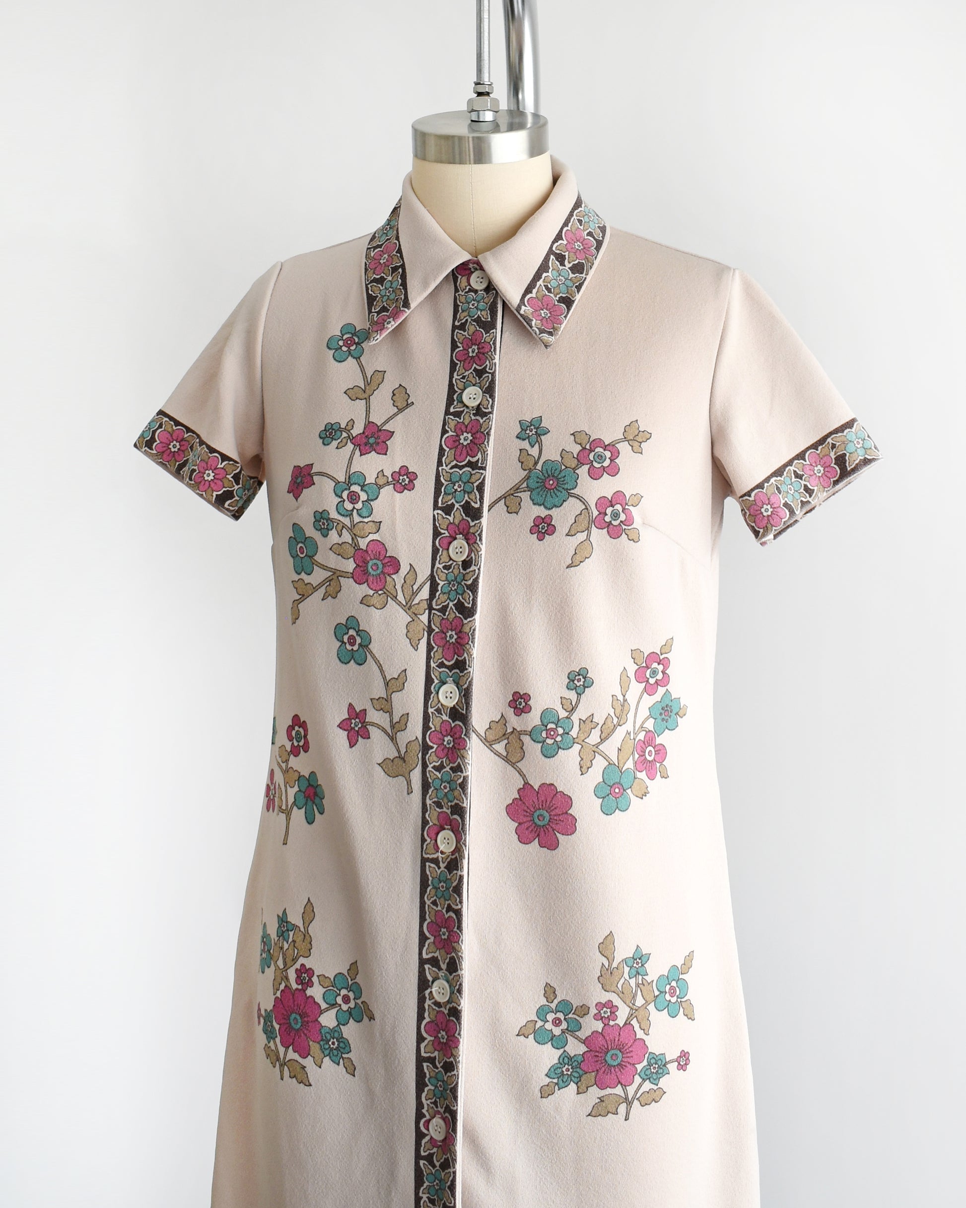 Side front view of a vintage 1970s light brown mod dress with a button front that features a blue and pink floral print 