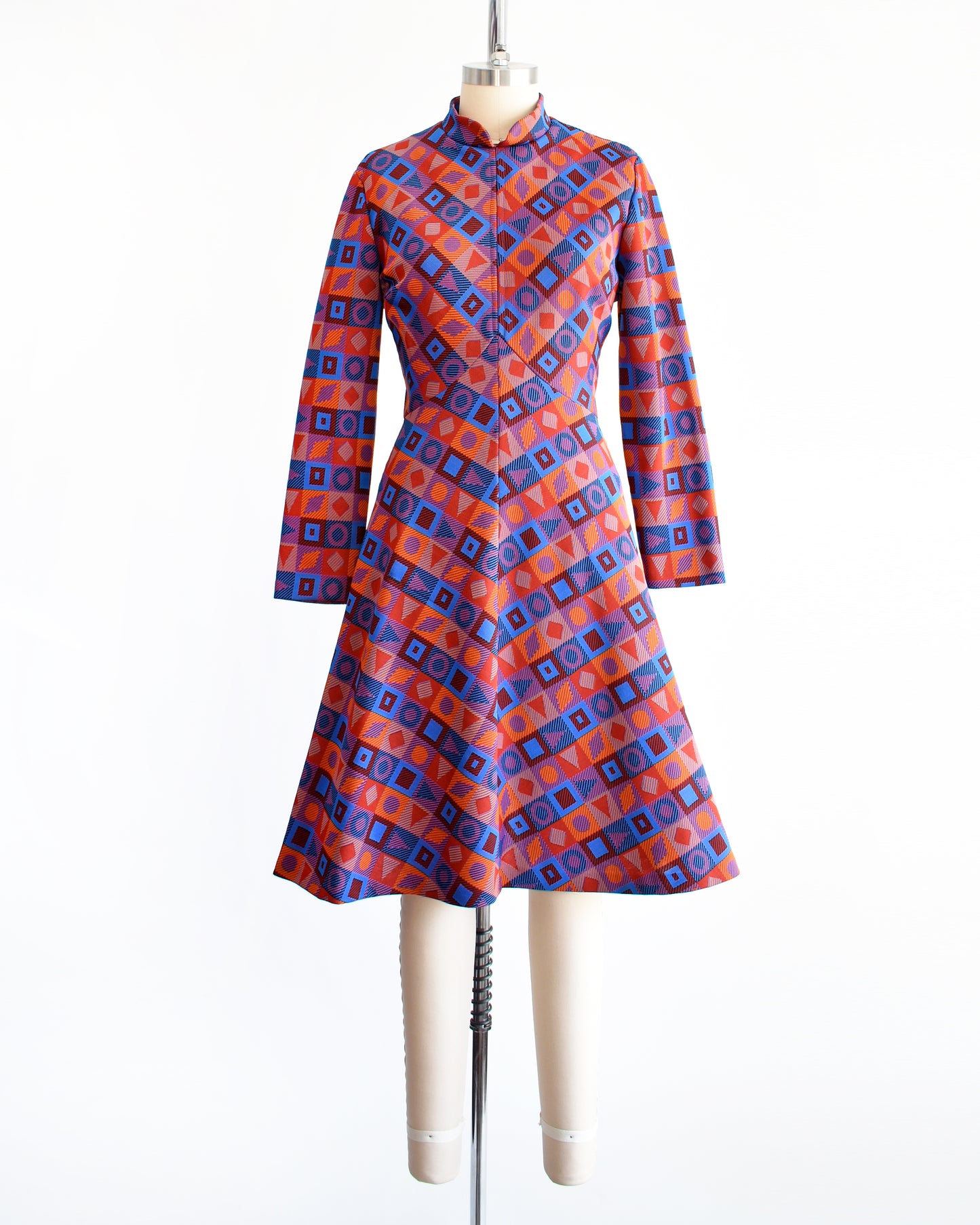 A vintage 1970s mod geometric print dress features a chevron pattern made up of orange, blue, black, and red squares, each with its own unique shape.
