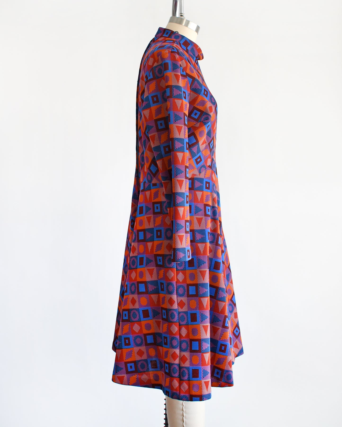 Side view of a vintage 1970s mod geometric print dress features a chevron pattern made up of orange, blue, black, and red squares, each with its own unique shape.