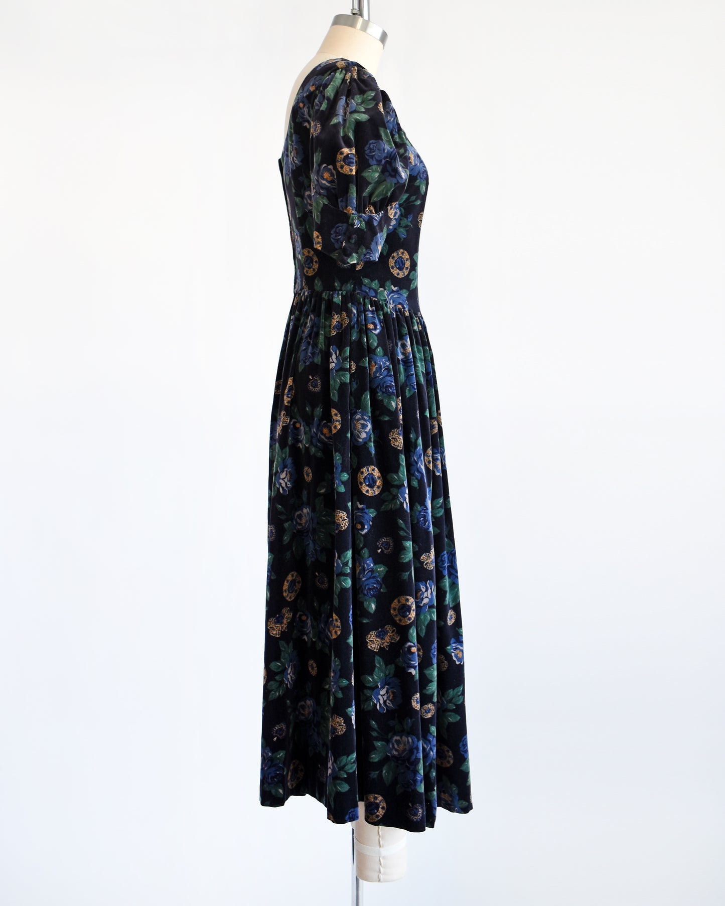 Side view of a vintage 1980s Laura Ashley dress. Black cotton velvet with a navy blue floral and metal gold jewels print.