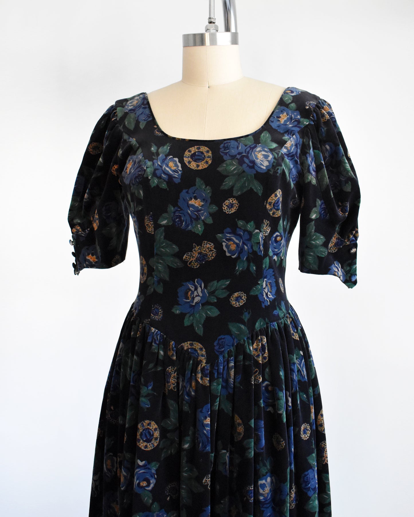 Side front view of a vintage 1980s Laura Ashley dress. Black cotton velvet with a navy blue floral and metal gold jewels print.