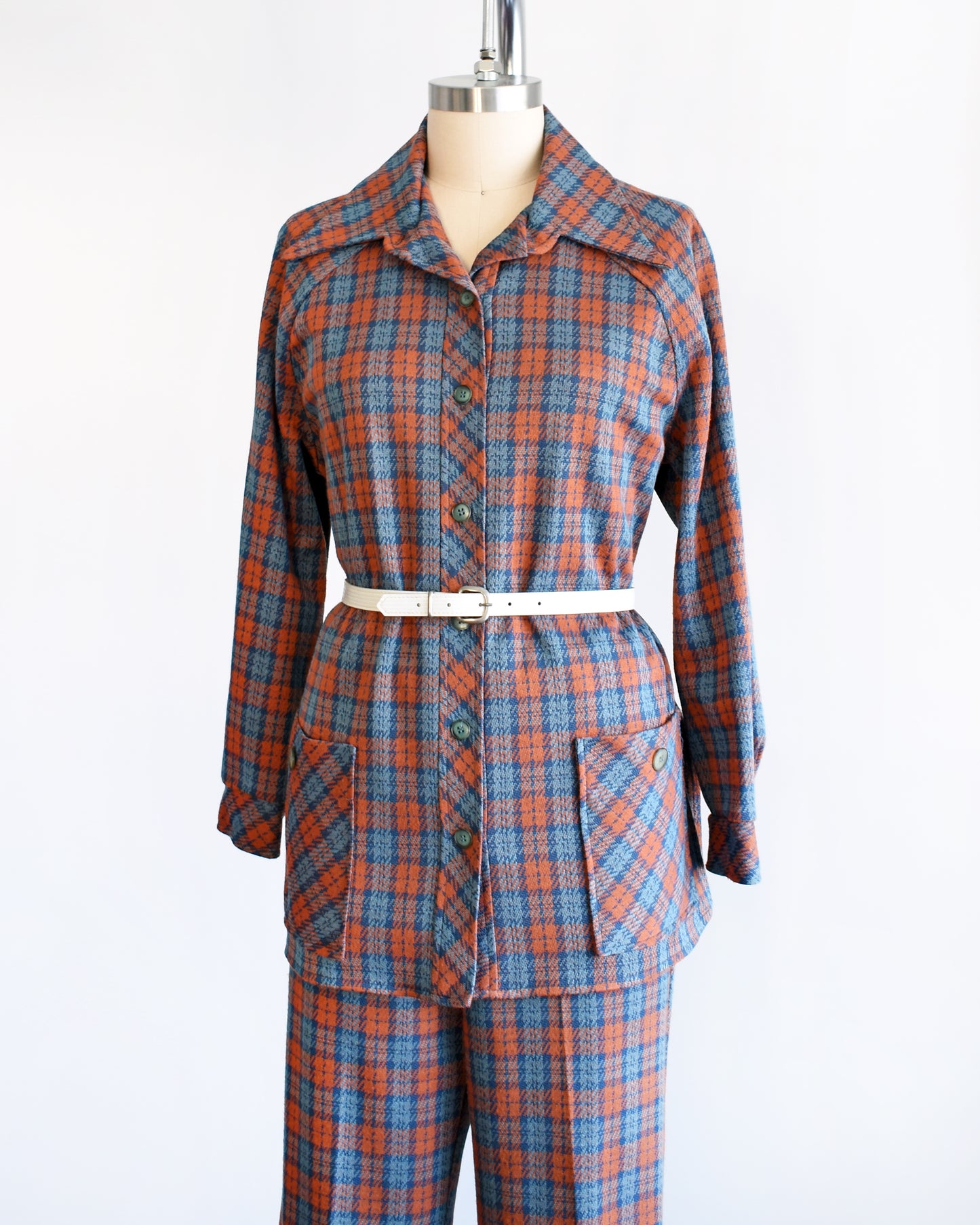 Side front view of a vintage 1970s blue and orange plaid pantsuit. This set includes a blue and orange plaid long sleeve blouse and matching wide leg pants. There is a white belt shown in this photo, but not included.