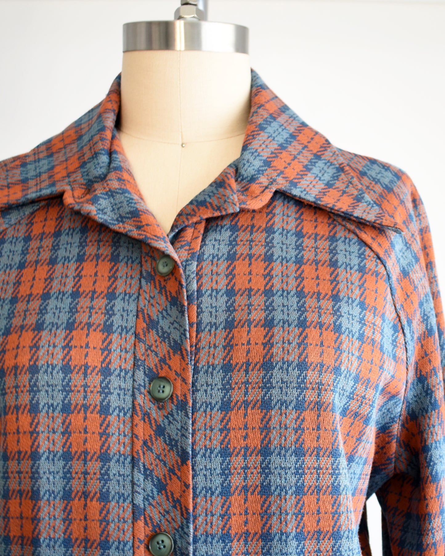Close up of the top which shows the orange and blue plaid, buttons, and butterfly collar