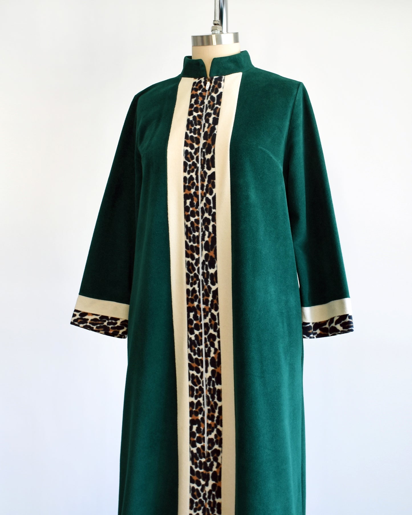 Side front view of a vintage 1970s robe by Vanity Fair that is a rich dark green with a white and leopard print stripe going down the front and matching stripes on the cuffs.