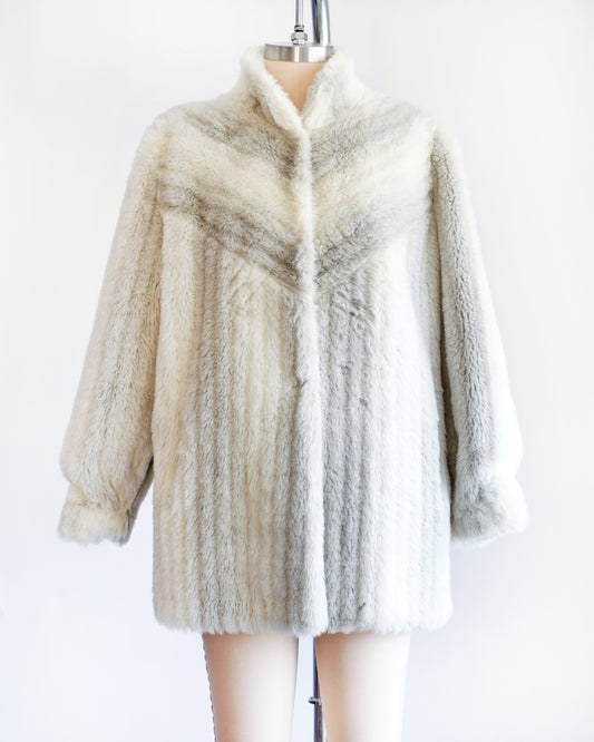 A vintage 70s/80s faux fur coat is made from a plush white faux fur with gray stripes, and features a stand-up collar with slightly puffed shoulders.