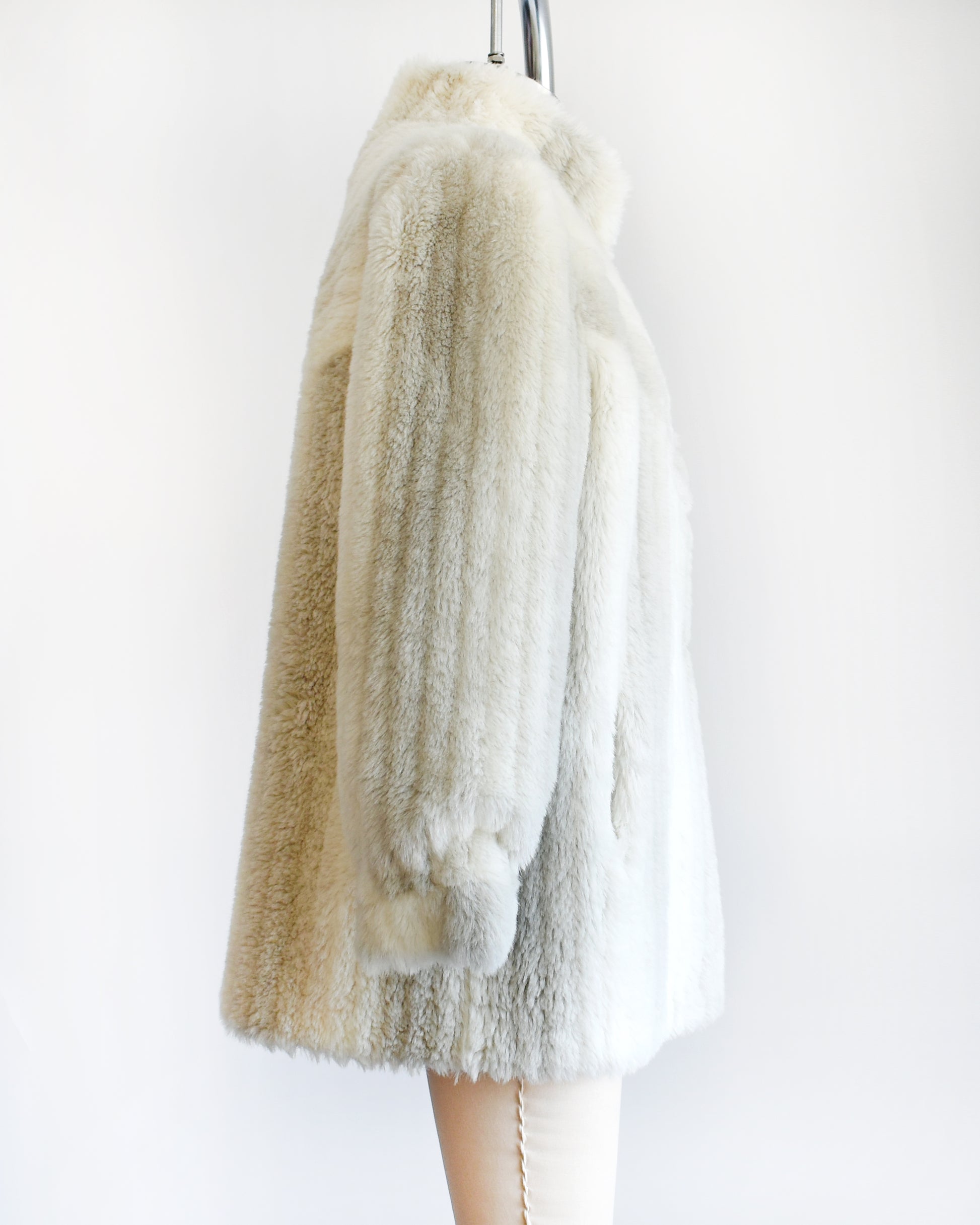 Side view of a vintage 70s/80s faux fur coat is made from a plush white faux fur with gray stripes, and features a stand-up collar with slightly puffed shoulders.