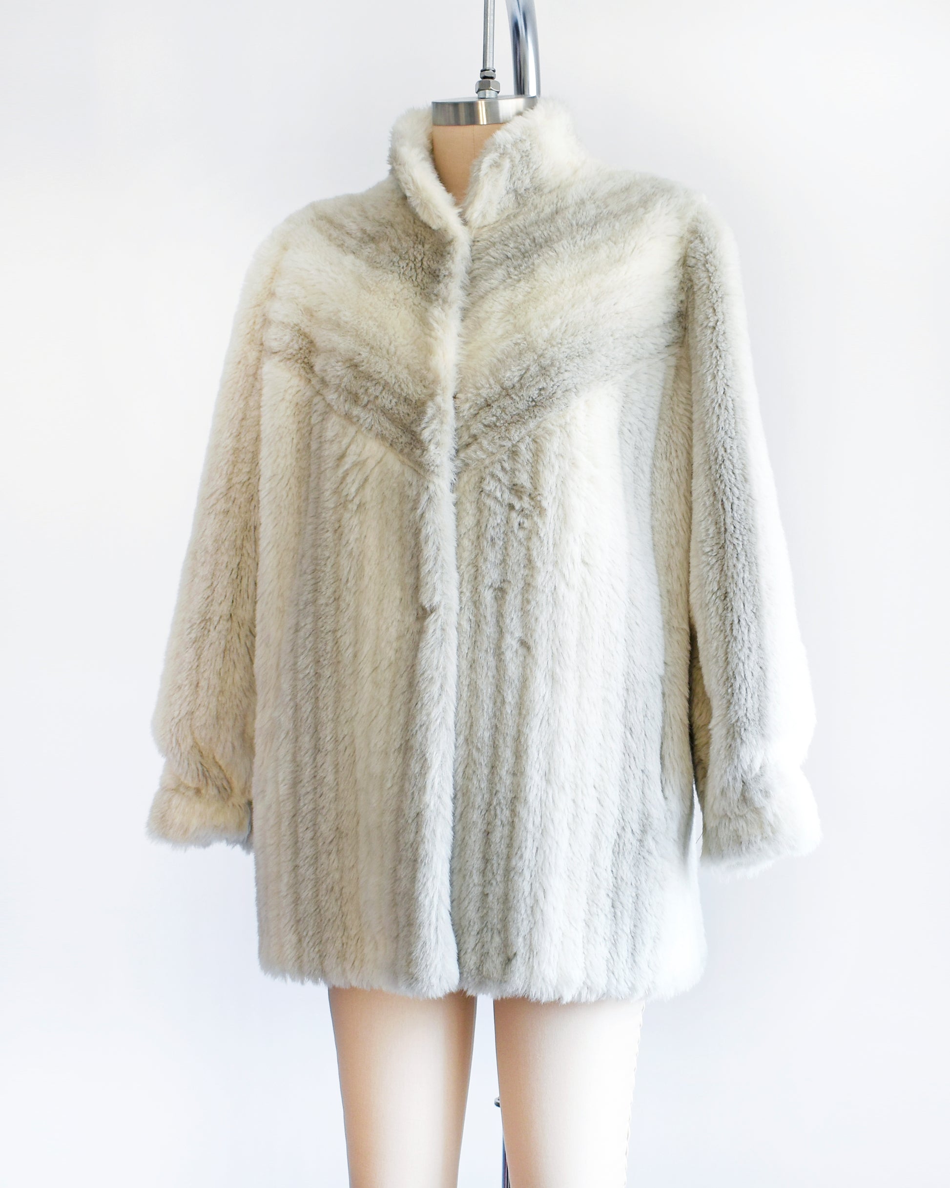 Side front view of a vintage 70s/80s faux fur coat is made from a plush white faux fur with gray stripes, and features a stand-up collar with slightly puffed shoulders.