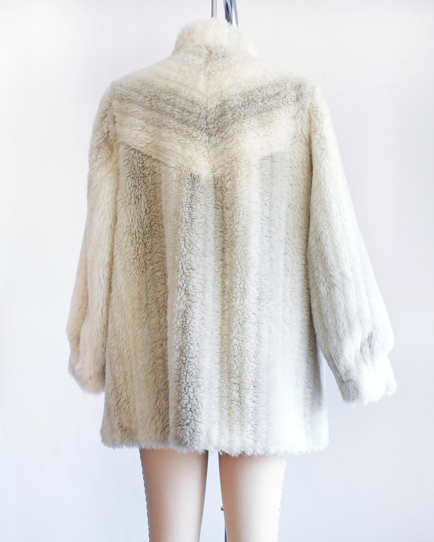 Back view of a vintage 70s/80s faux fur coat is made from a plush white faux fur with gray stripes, and features a stand-up collar with slightly puffed shoulders.
