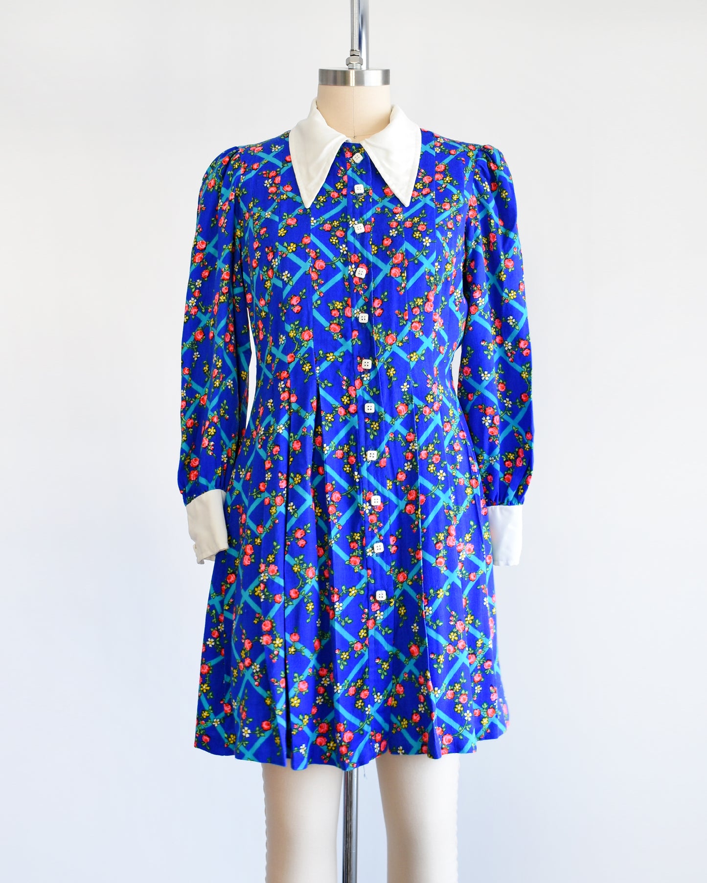 A vintage 1970s blue floral mini dress that has a white collar with matching cuffs, and white buttons down the front.
