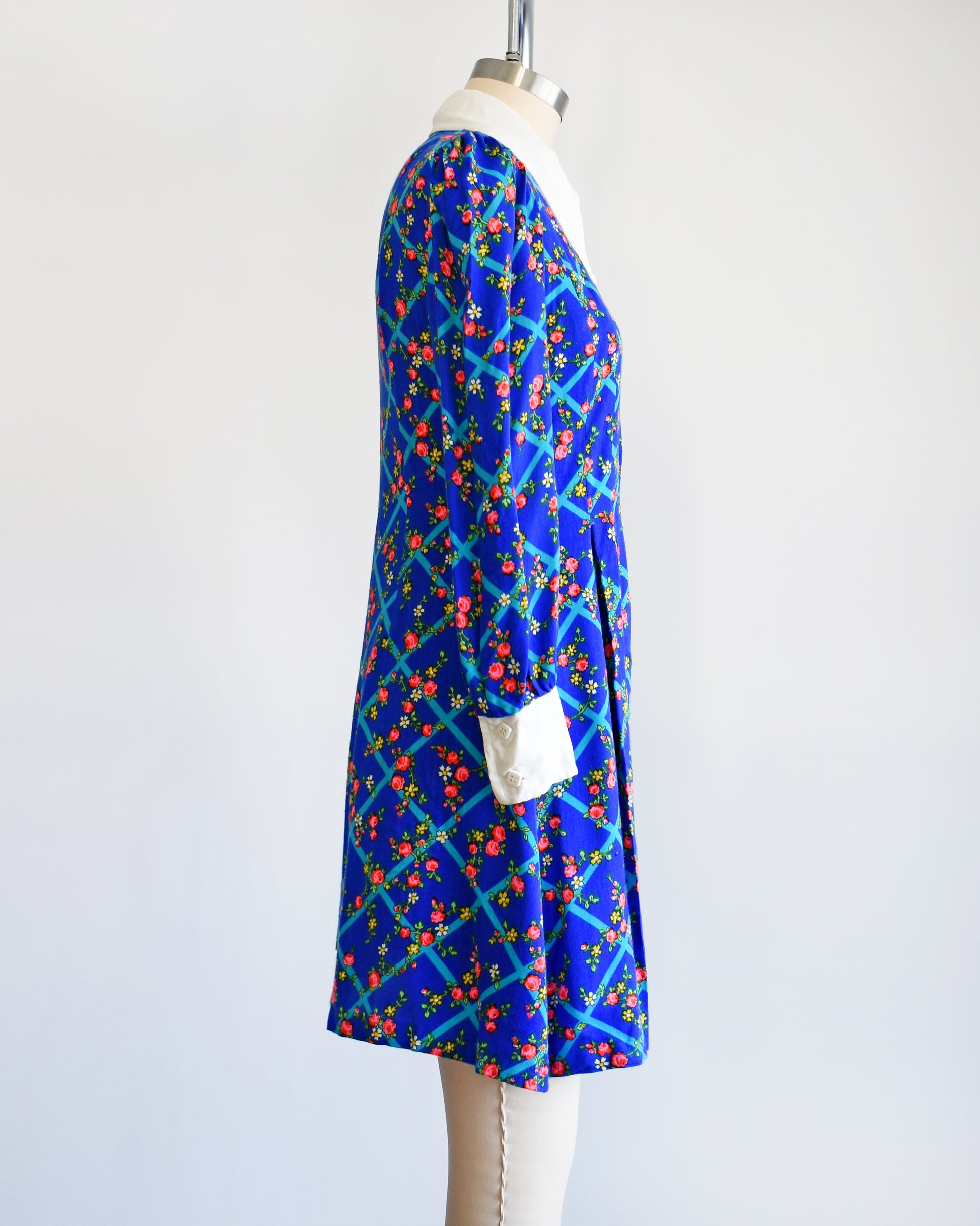 Side view of a vintage 1970s blue floral mini dress that has a white collar with matching cuffs, and white buttons down the front.