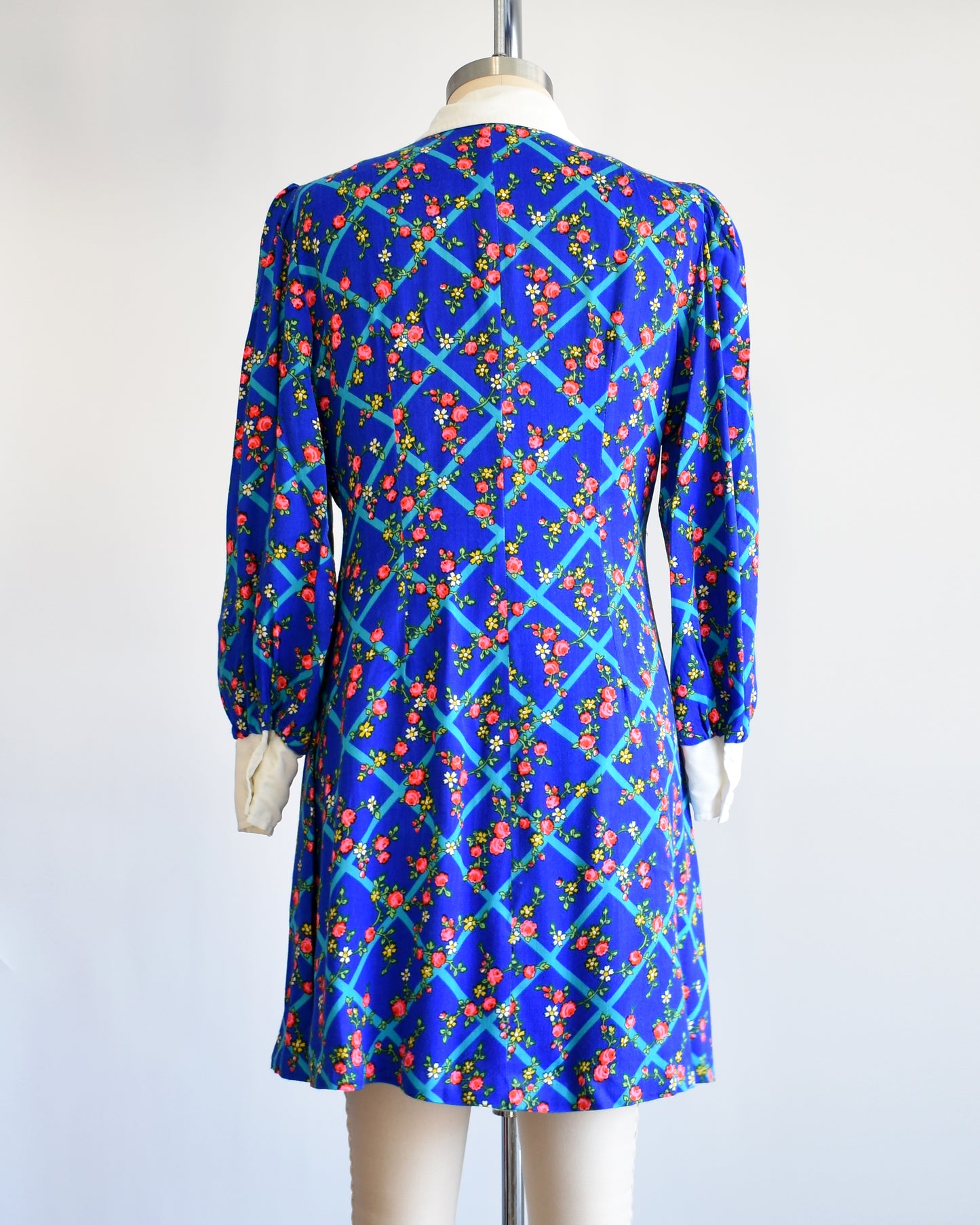 Back view of a vintage 1970s blue floral mini dress that has a white collar with matching cuffs, and white buttons down the front.