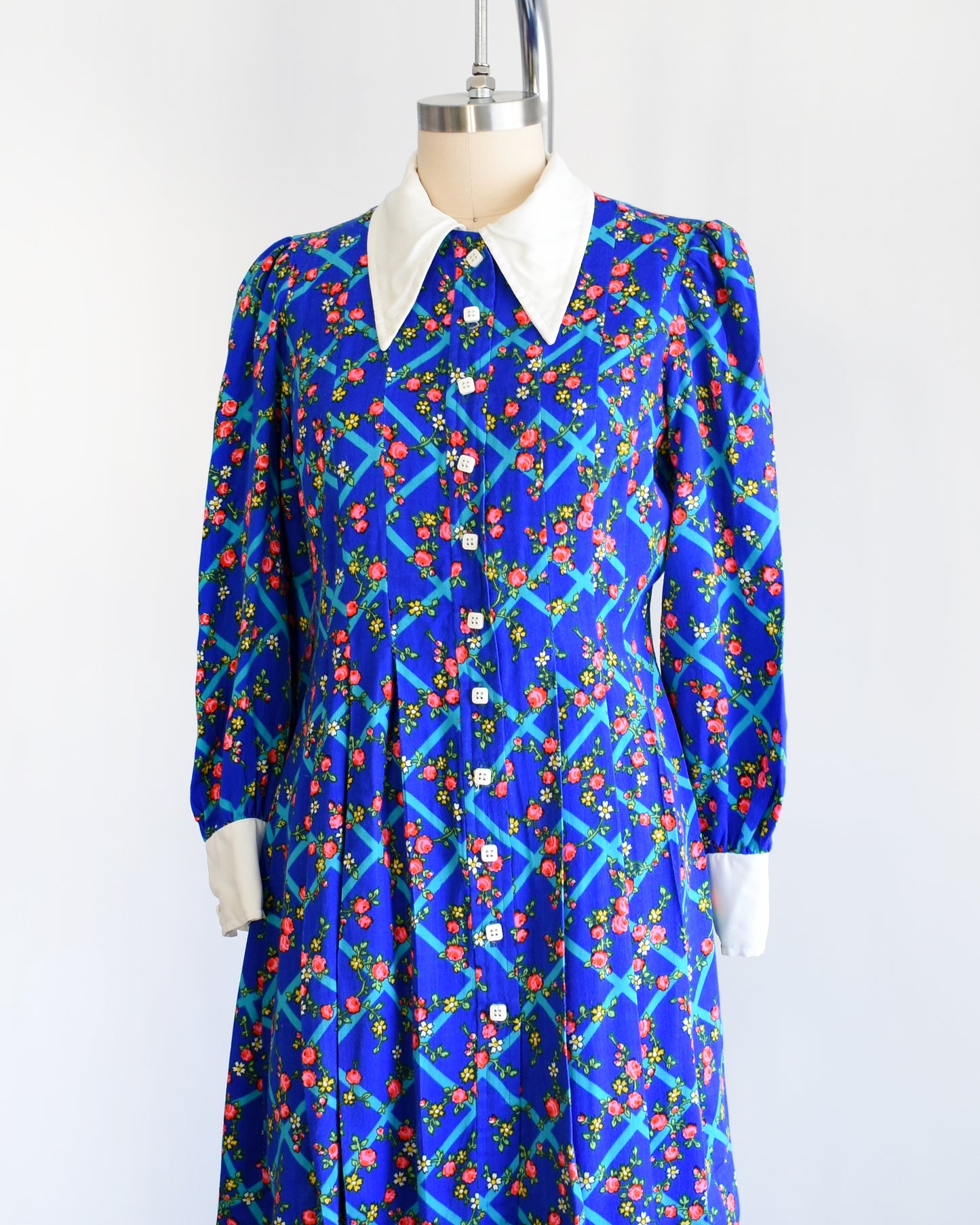 Side front view of a vintage 1970s blue floral mini dress that has a white collar with matching cuffs, and white buttons down the front.