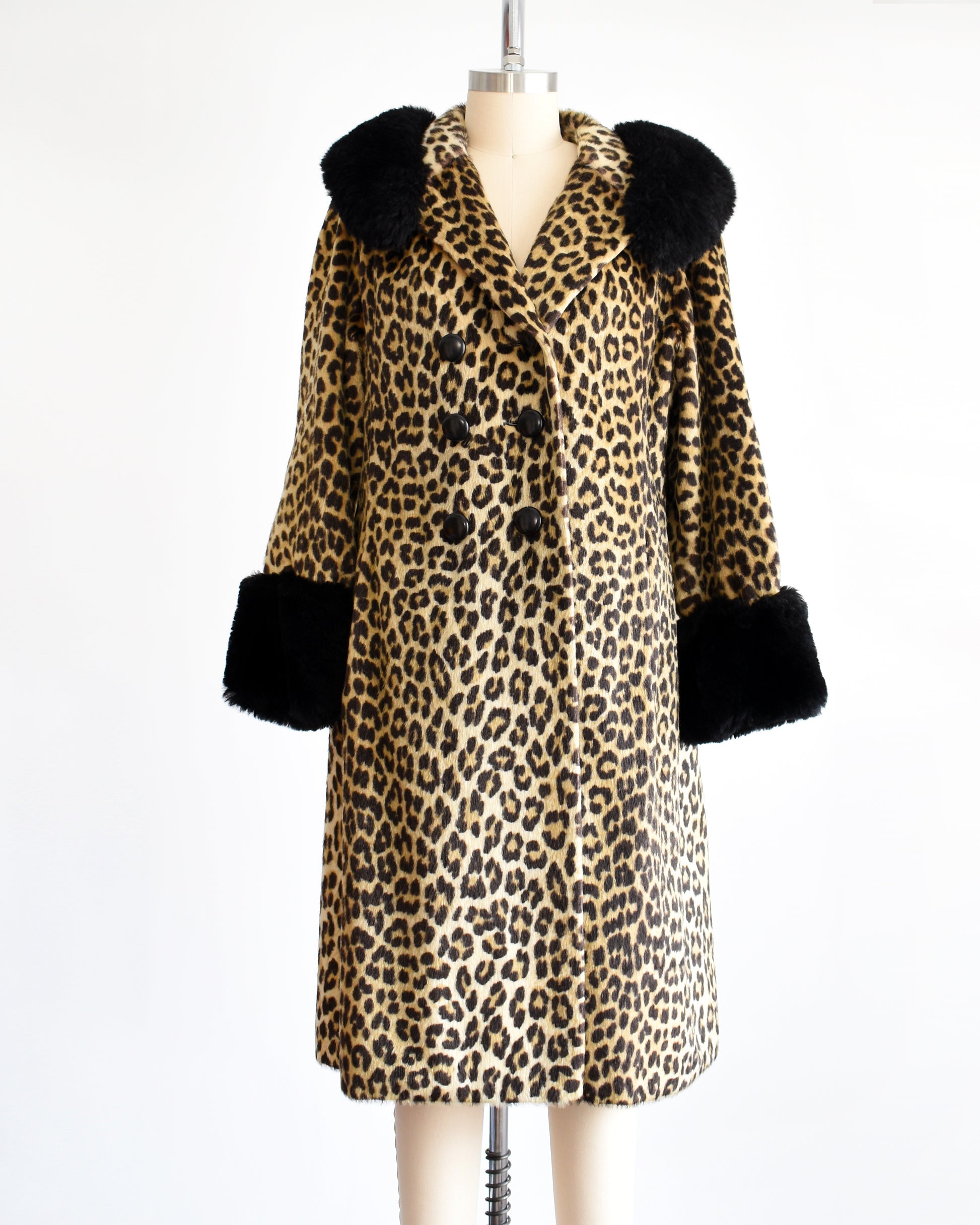 A vintage 1960s faux fur leopard print coat. Black plush trim along the collar and on the cuffs. The top button is unbuttoned.