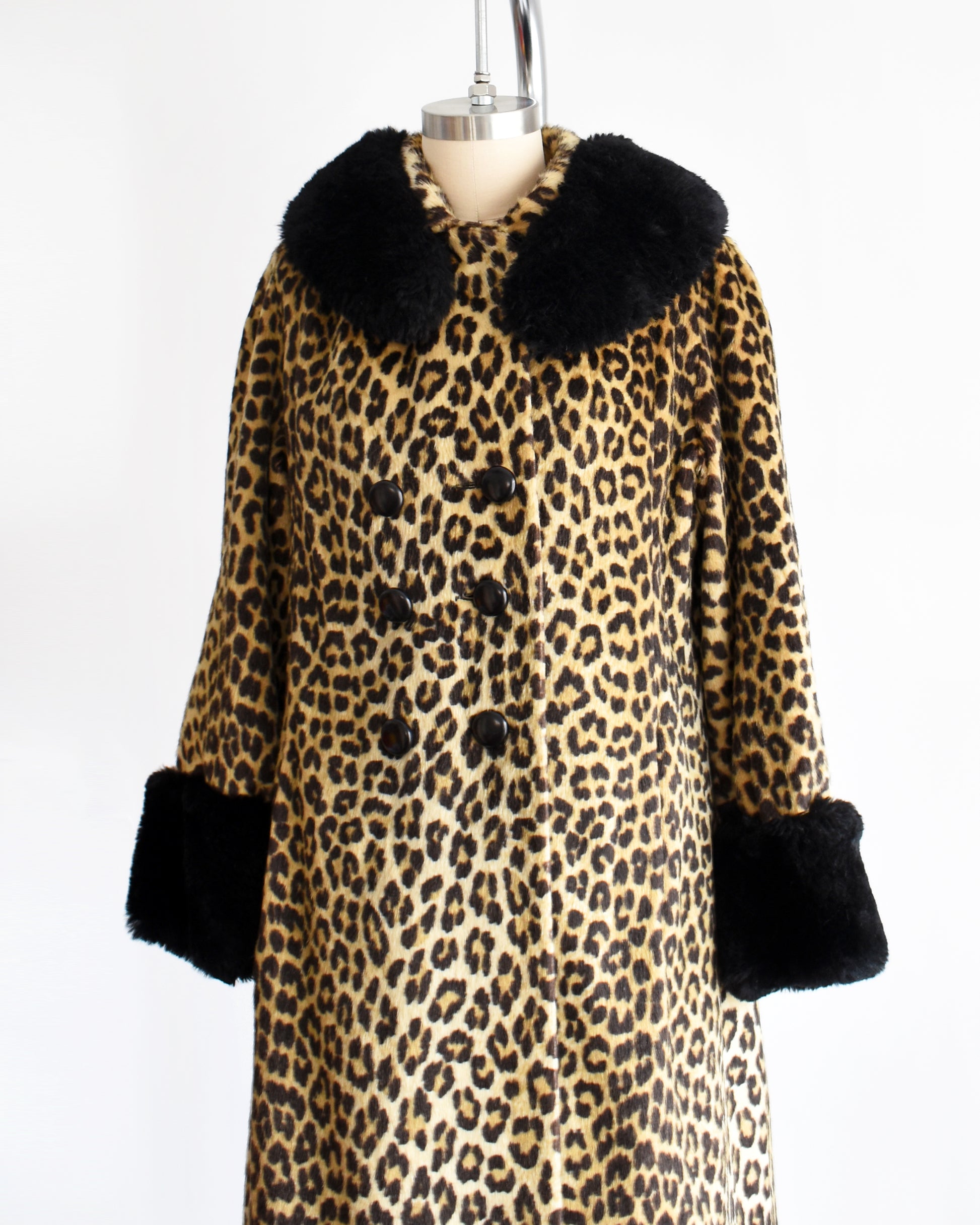 Side front view of a vintage 1960s faux fur leopard print coat. Black plush trim along the collar and on the cuffs. The coat is buttoned all the way up in this photo.