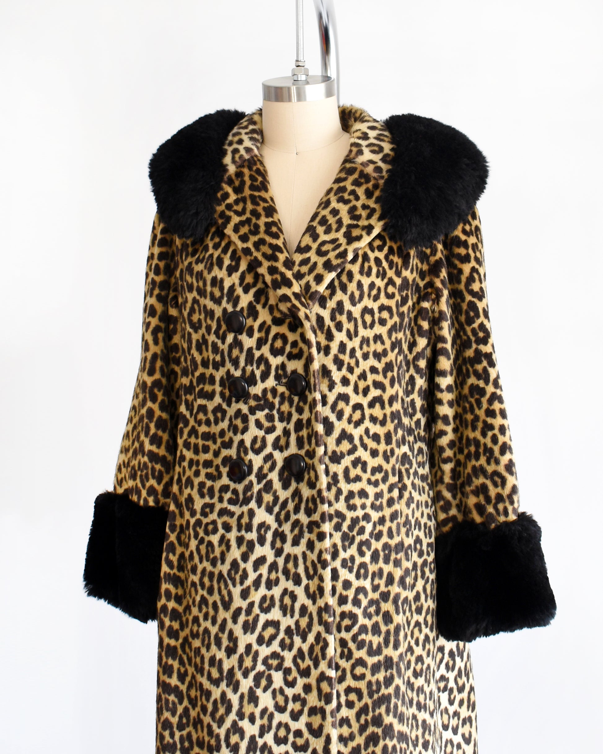 Side front view of a vintage 1960s faux fur leopard print coat. Black plush trim along the collar and on the cuffs. The top button is unbuttoned in this photo.
