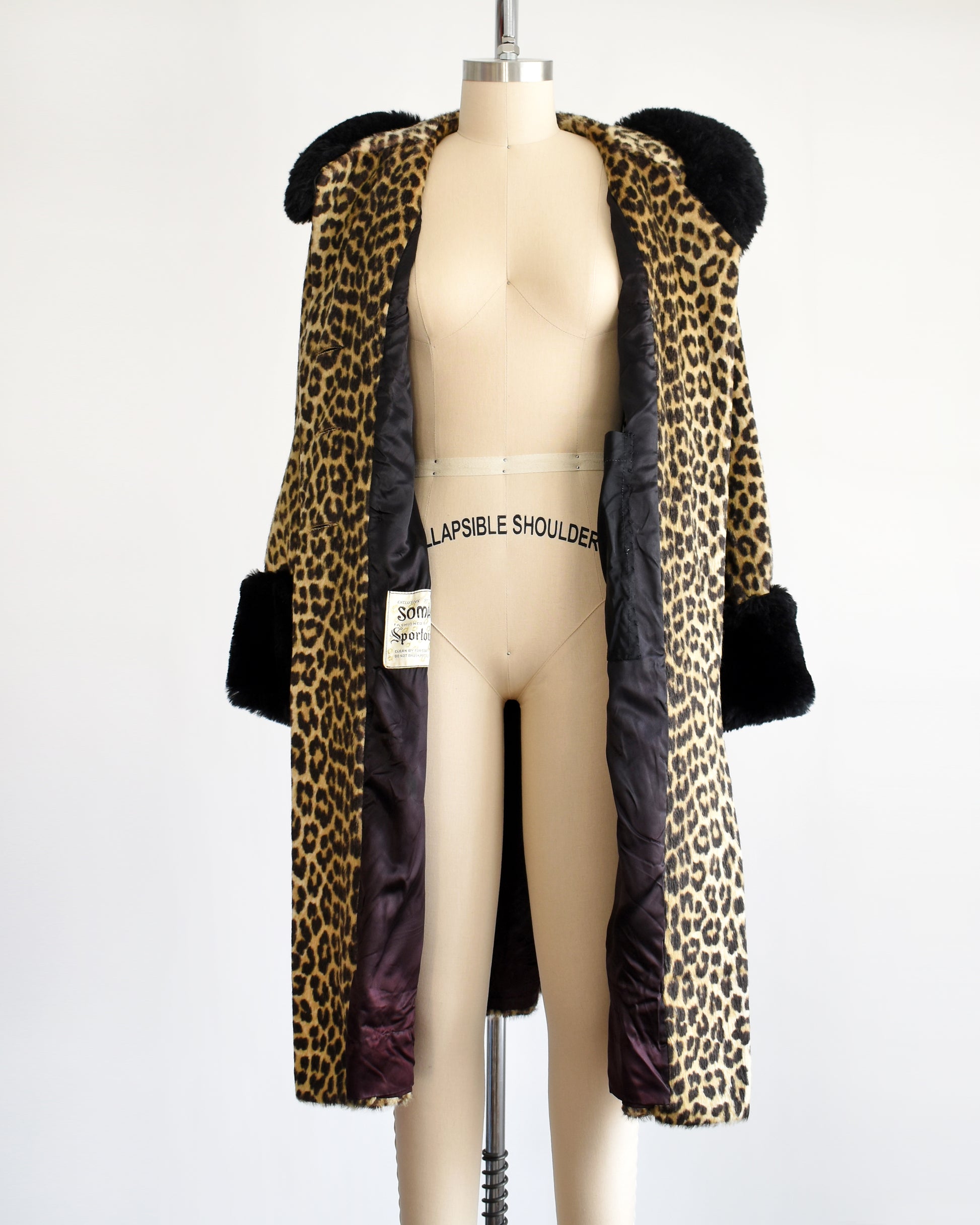 A vintage 1960s faux fur leopard print coat. Black plush trim along the collar and on the cuffs. The coat is open in this photo