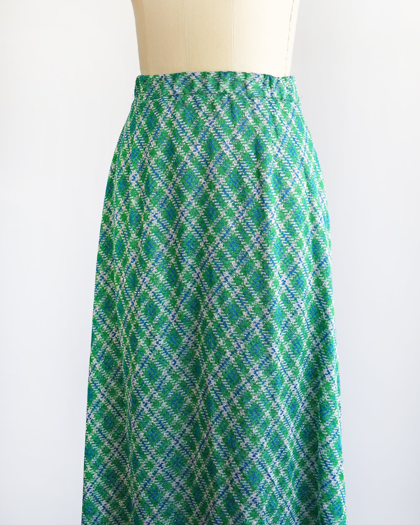 Side front view of a vintage 1970s maxi skirt that features festive green, blue, and white plaid fabric with silver metallic threads.