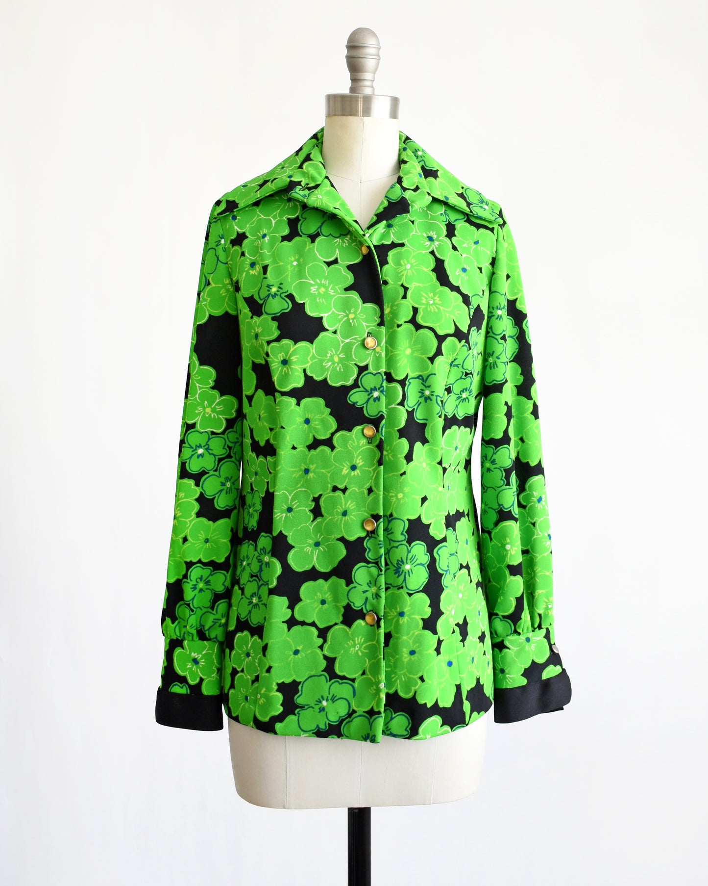 A vintage 1970s green and black floral blouse with yellow buttons down the front. The top button is unbuttoned.