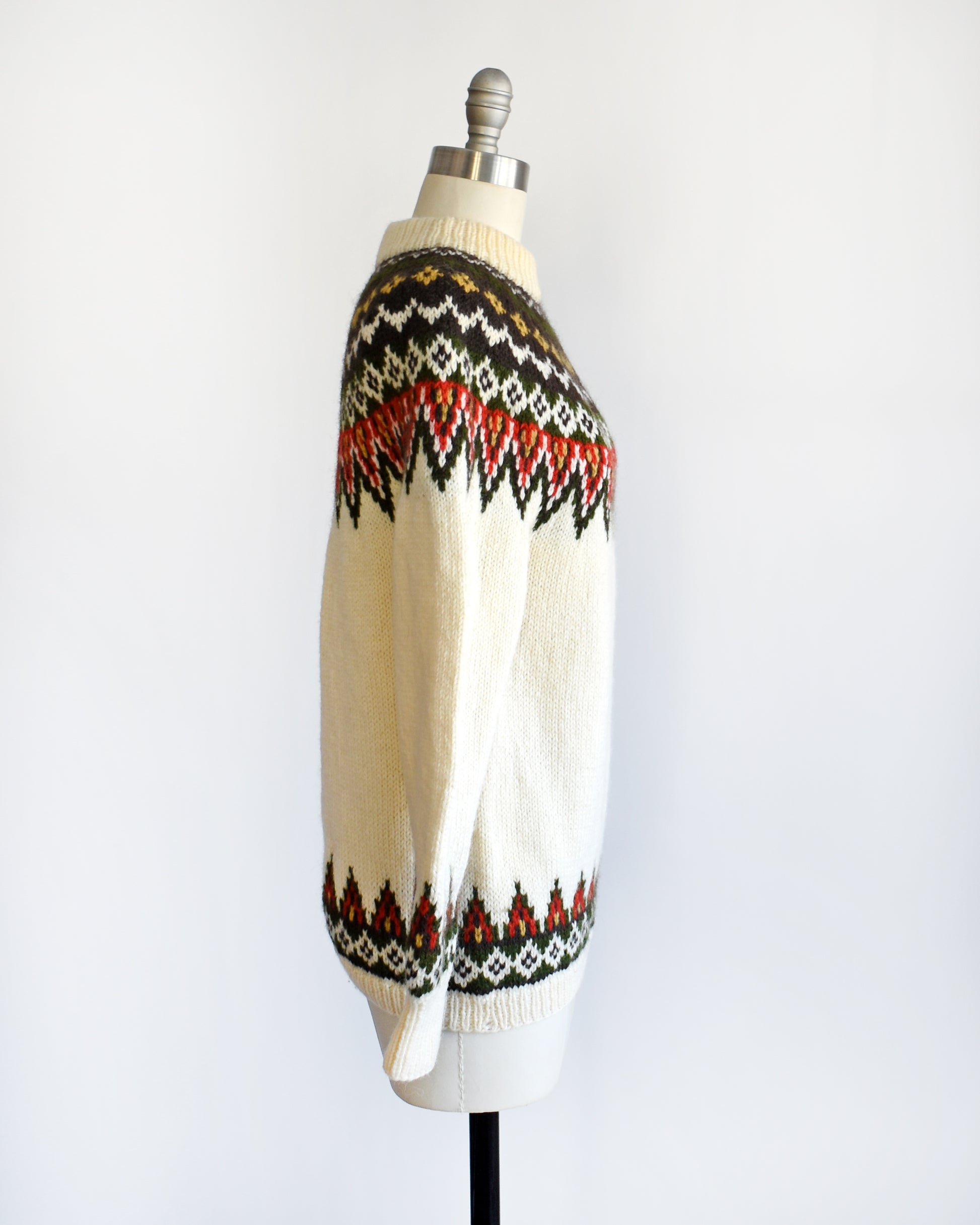 Side view of a vintage 1970s cream wool Nordic sweater with a brown, dark green, yellow, and red orange Fair Isle pattern around the collar and complimentary pattern on the hem and cuffs.
