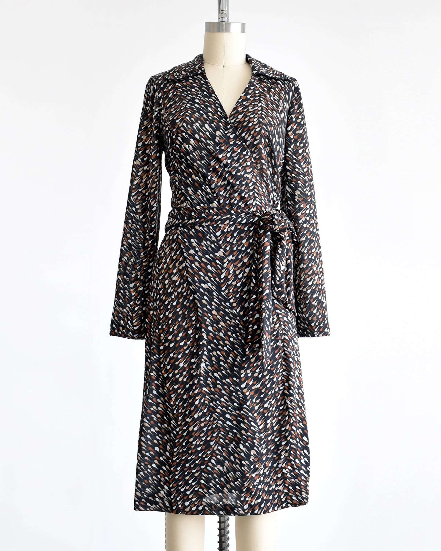 A vintage 1970s black wrap dress that has brown and white drop print, tie waist, and long sleeves.