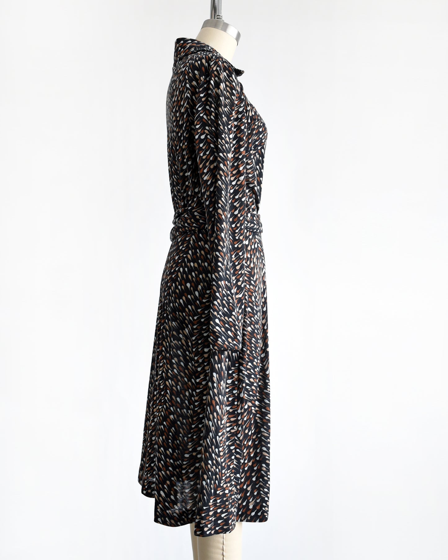 side view of a vintage 1970s black wrap dress that has brown and white drop print, tie waist, and long sleeves.