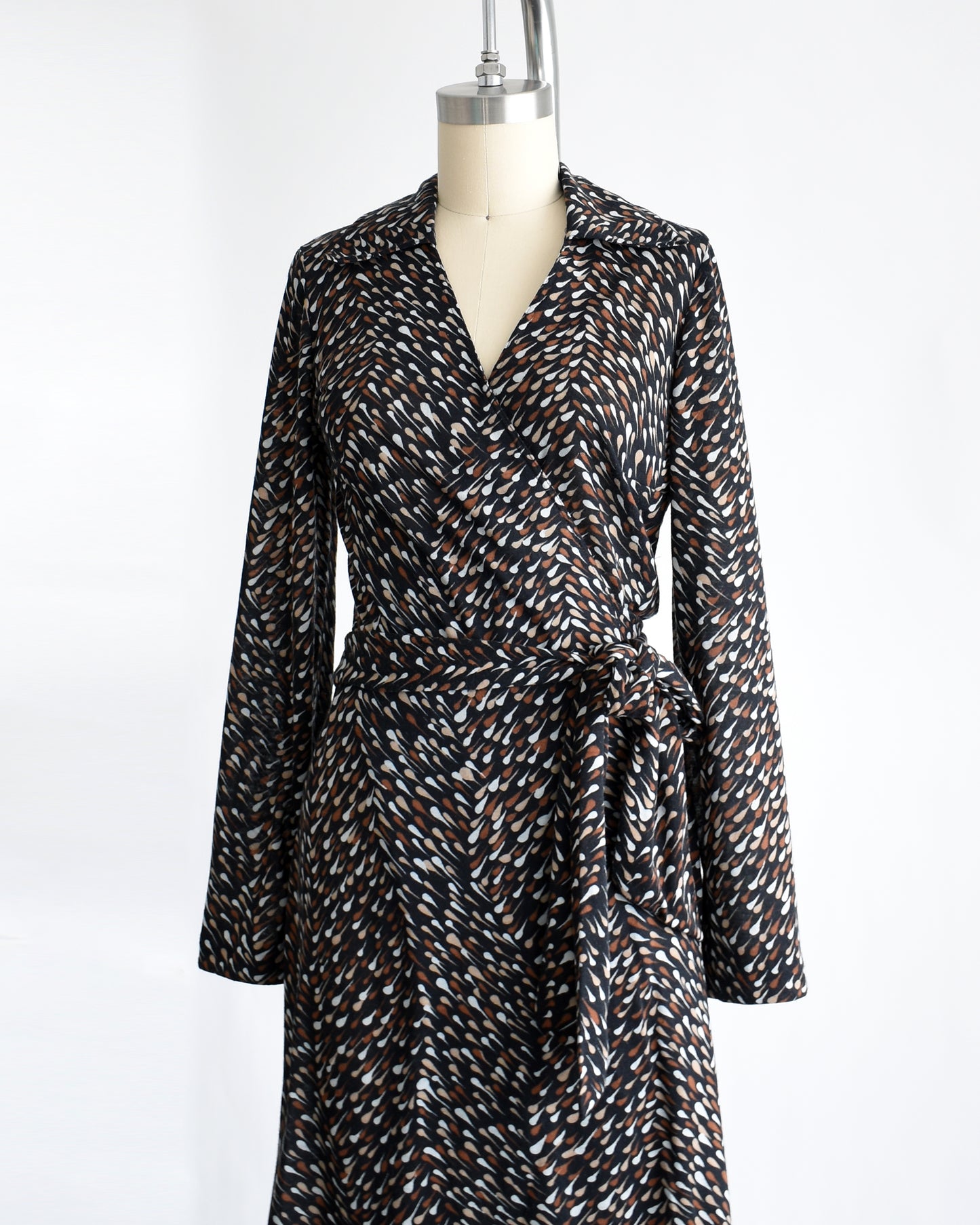 side front view of a vintage 1970s black wrap dress that has brown and white drop print