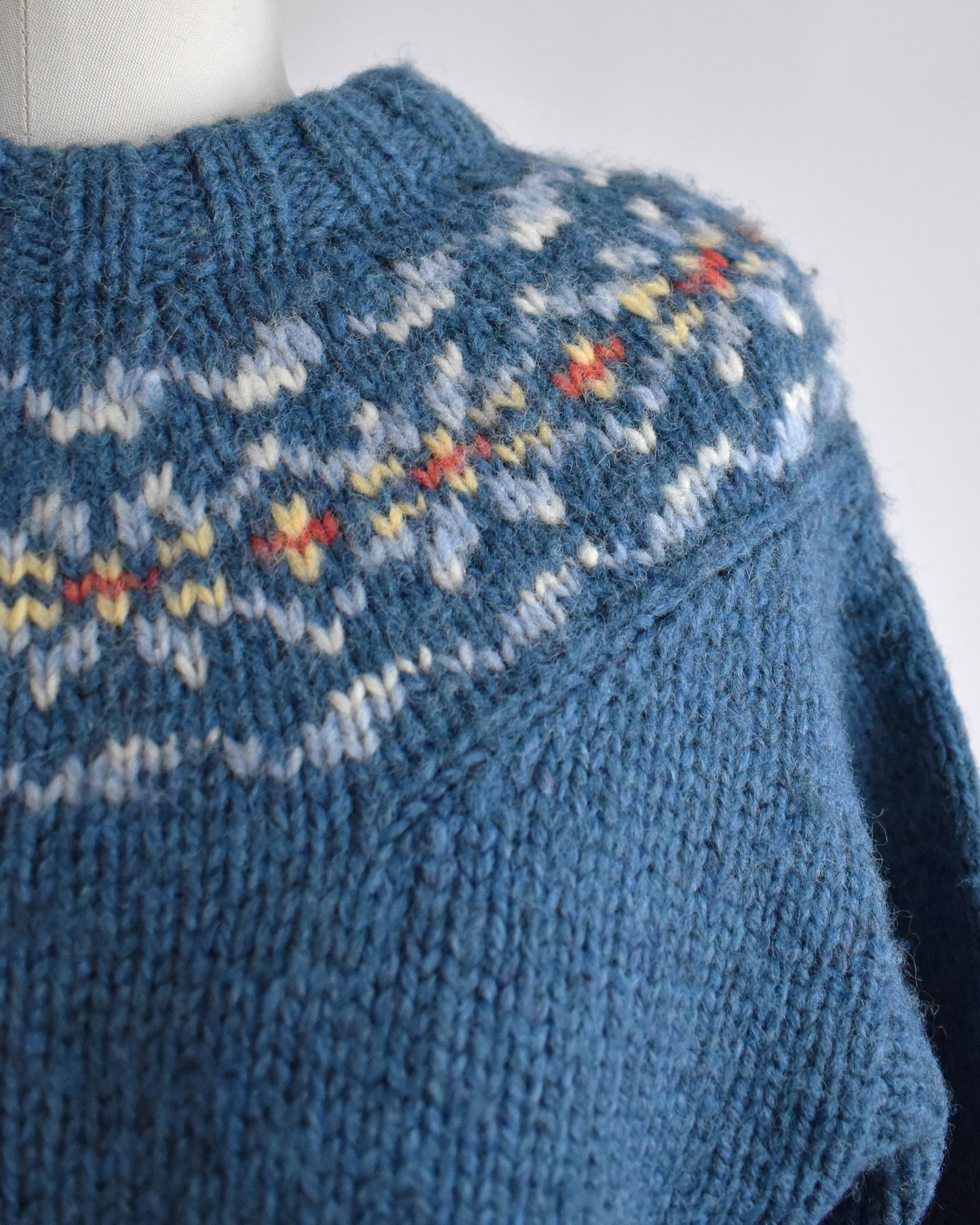 Close-up of a blue knitted sweater with a patterned collar on a white background