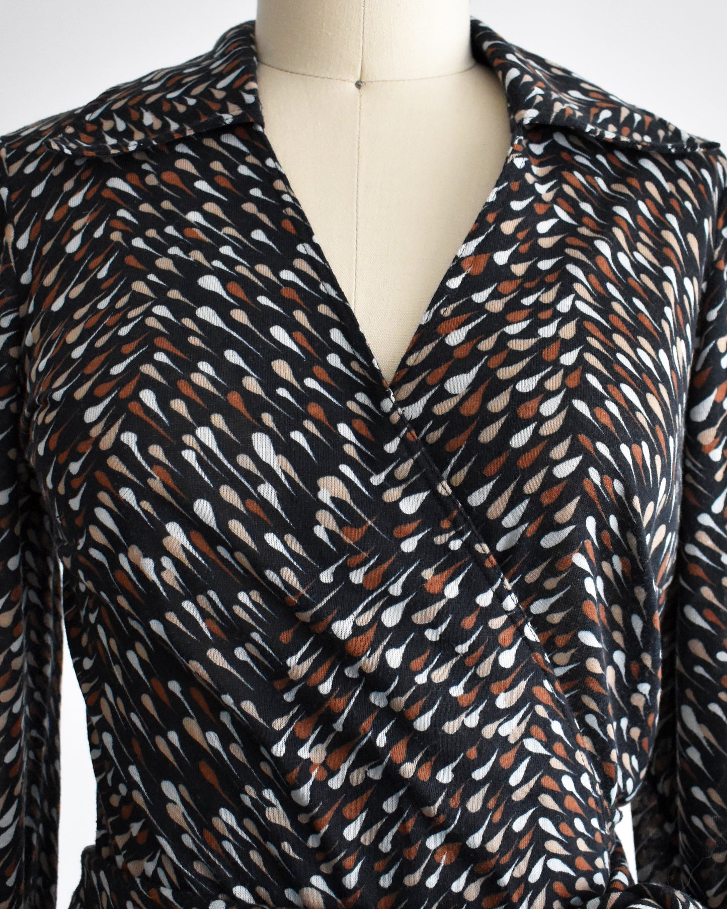 close up of the v-neckline on a vintage 1970s black wrap dress that has brown and white drop print