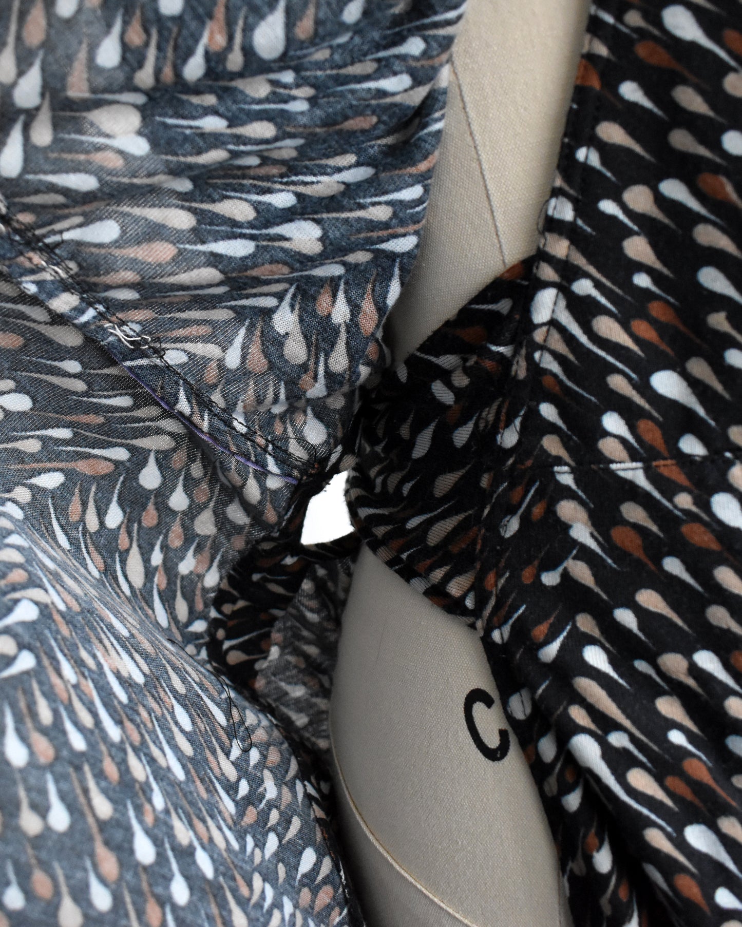 close up view of the inside wrap slit of a vintage 1970s black wrap dress that has brown and white drop print