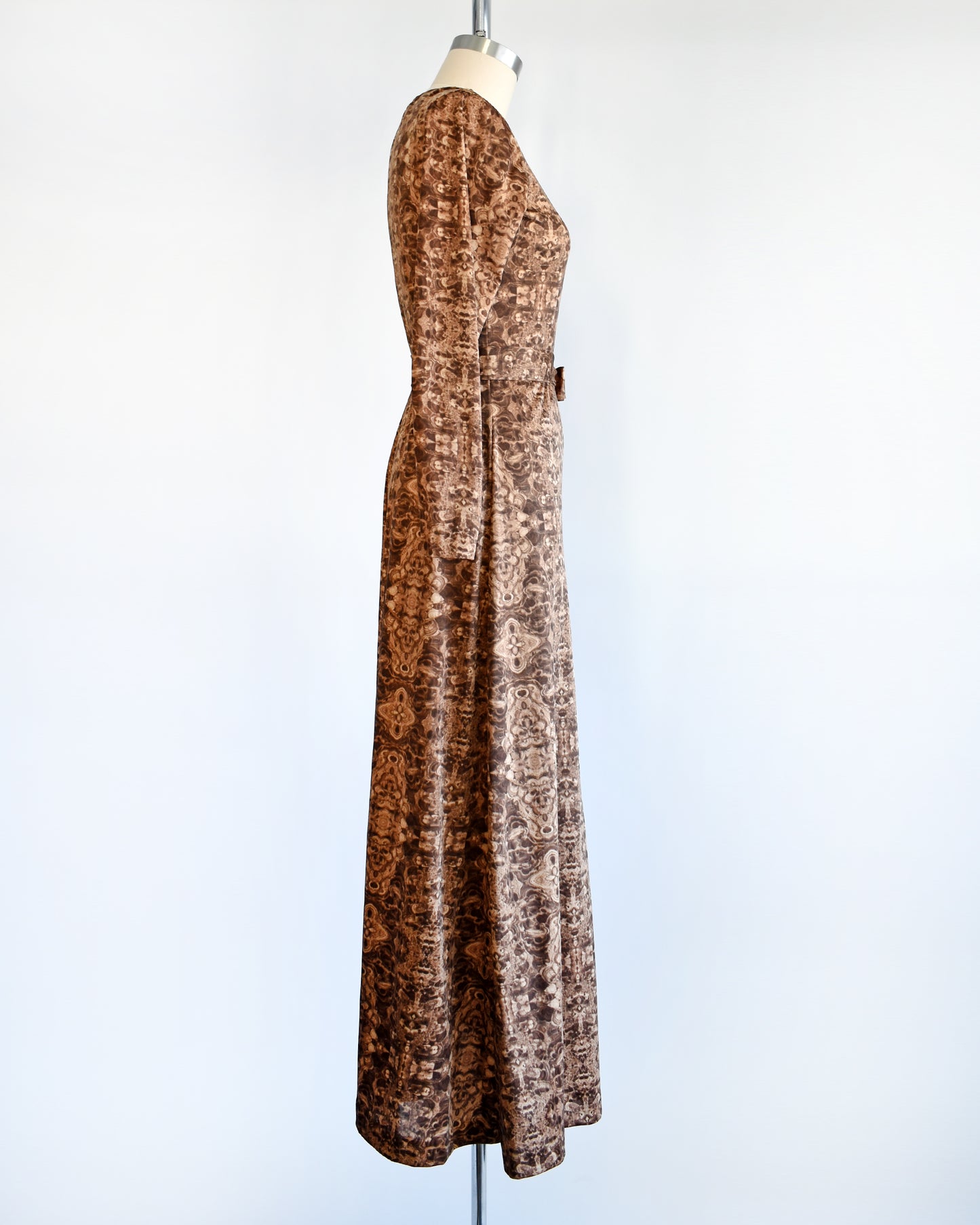 Side view of a vintage 1970s long sleeve maxi dress which features a psychedelic kaleidoscope pattern in light and dark brown.