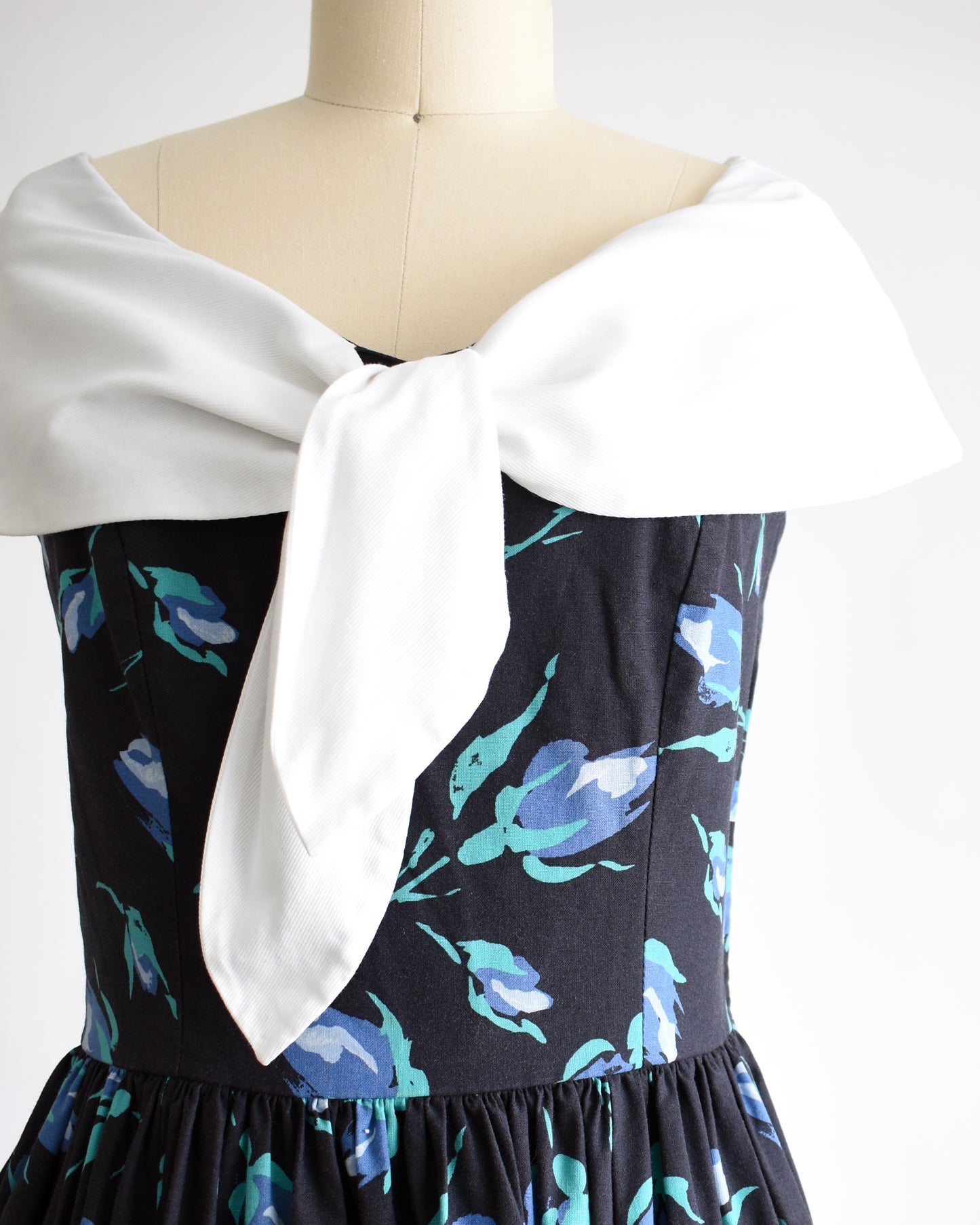 close up of the bodice of a vintage 1980s Laura Ashley dress that has a black and blue floral pattern and large white shawl collar.