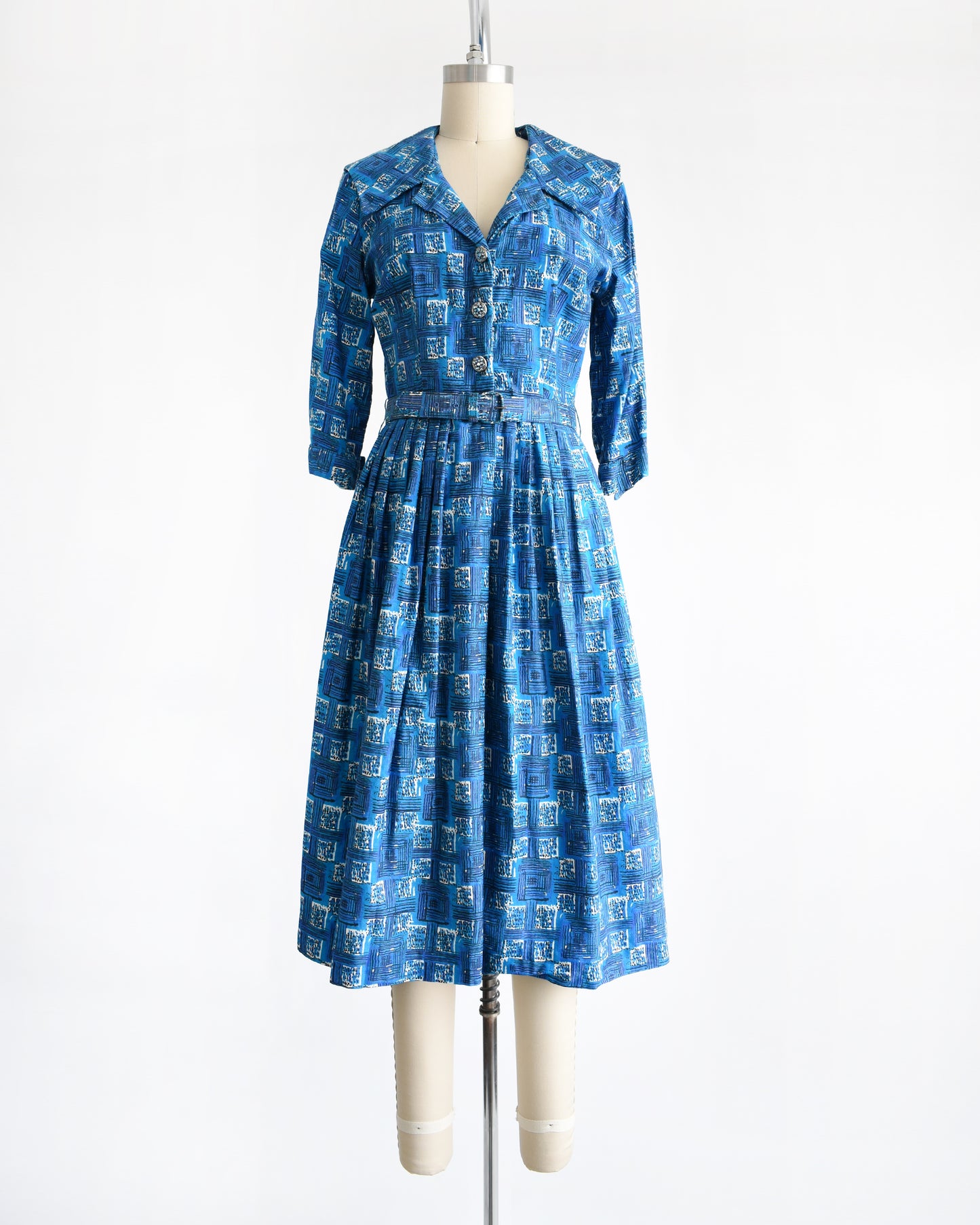 a vintage 1960s blue cotton day dress that has an abstract geometric print, rhinestone buttons, and matching belt