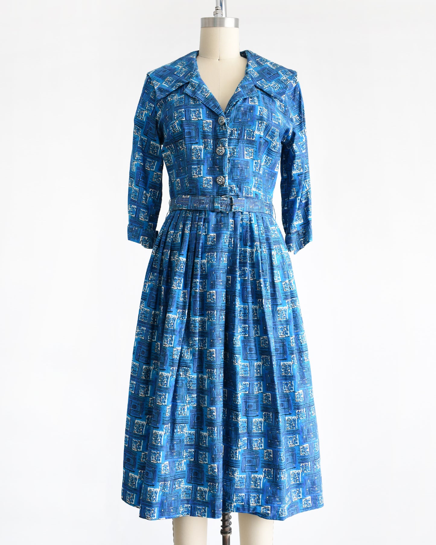 a vintage 1960s blue cotton day dress that has an abstract geometric print, rhinestone buttons, and matching belt