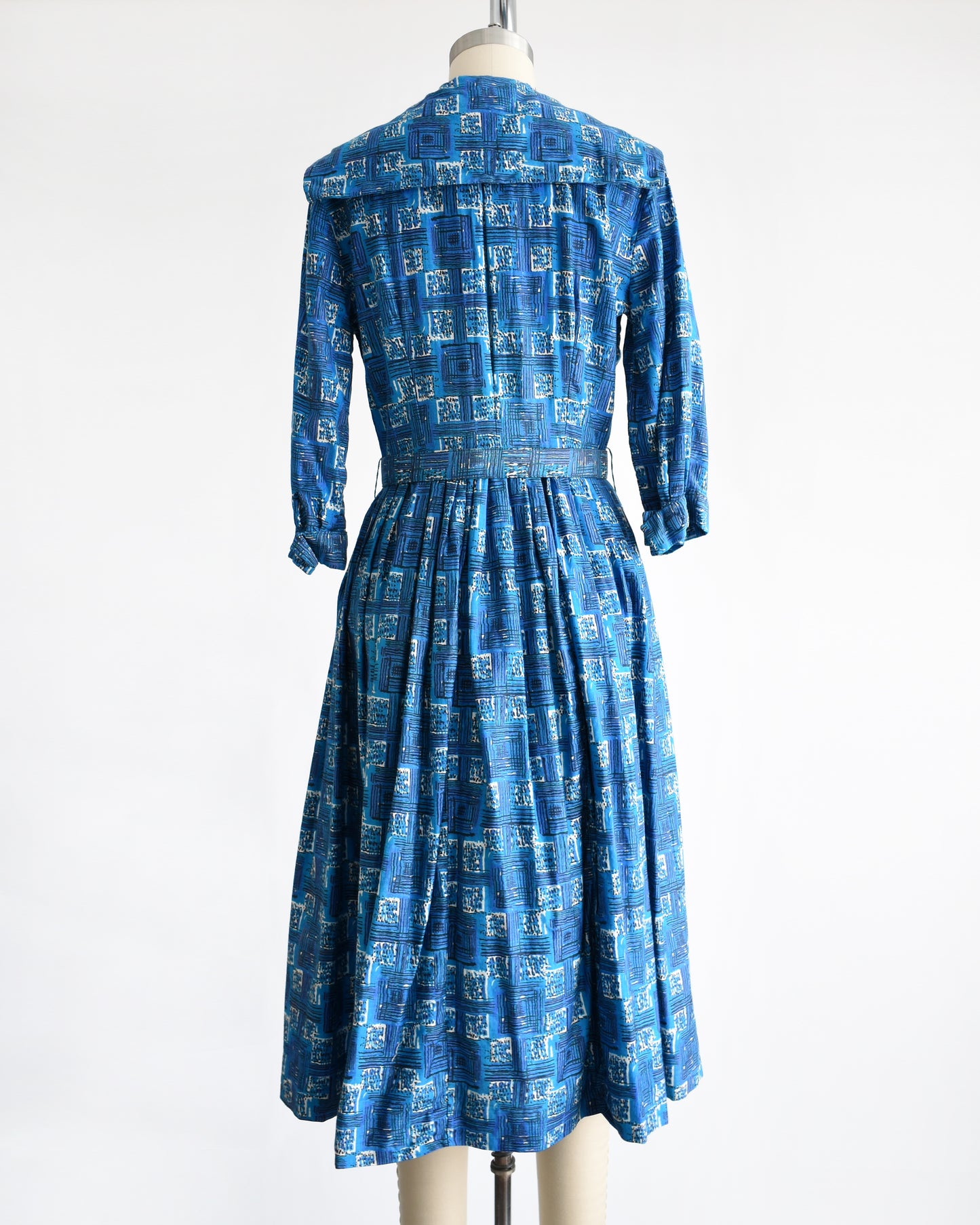 back view of a vintage 1960s blue cotton day dress that has an abstract geometric print, rhinestone buttons, and matching belt