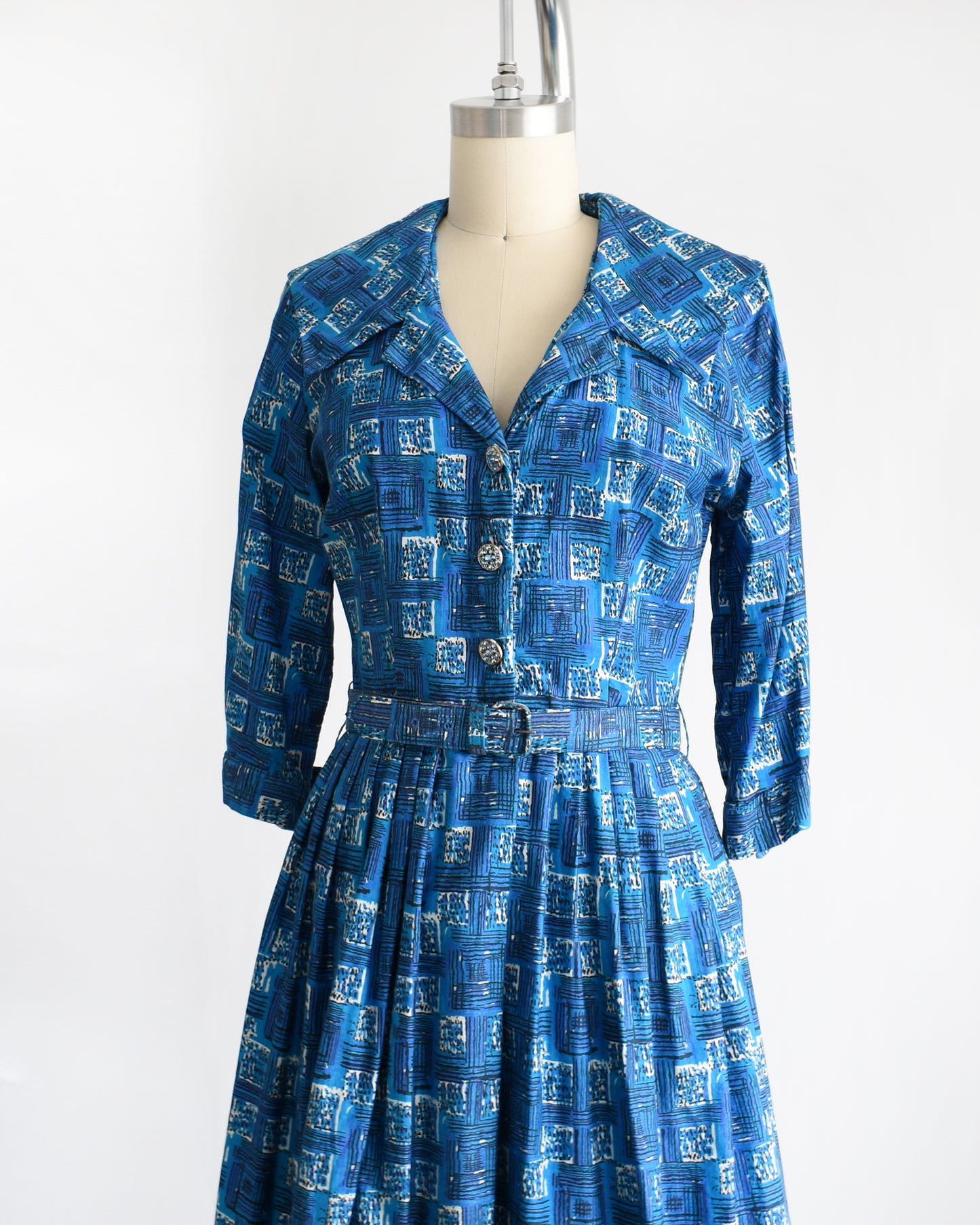 side front view of a vintage 1960s blue cotton day dress that has an abstract geometric print, rhinestone buttons, and matching belt