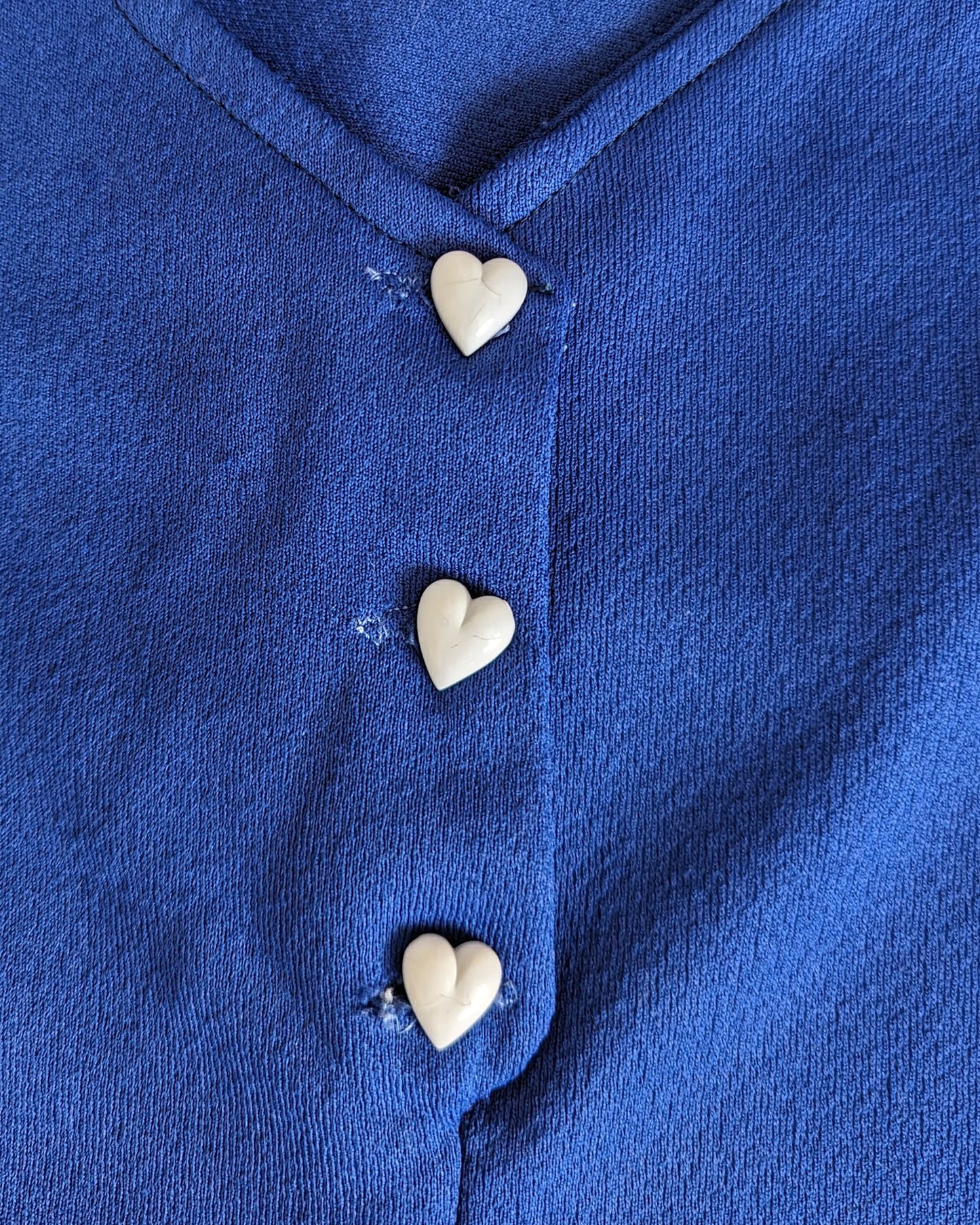 close up of the neckline and white heart buttons. there are small cracks on the buttons from age