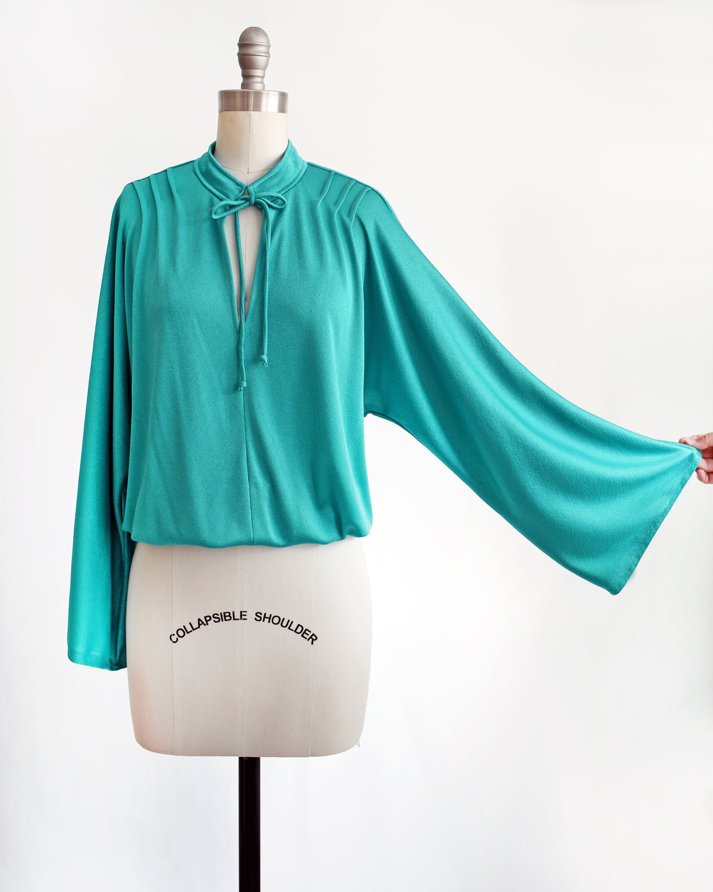 a vintage 1970s teal bell sleeve blouse that has the sleeve pulled