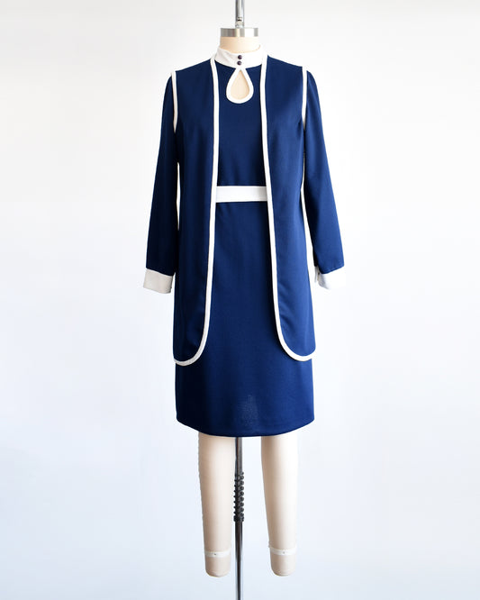 A late 1960s to early 1970s mod two piece set features a navy blue long sleeve dress and matching vest and white belt.
