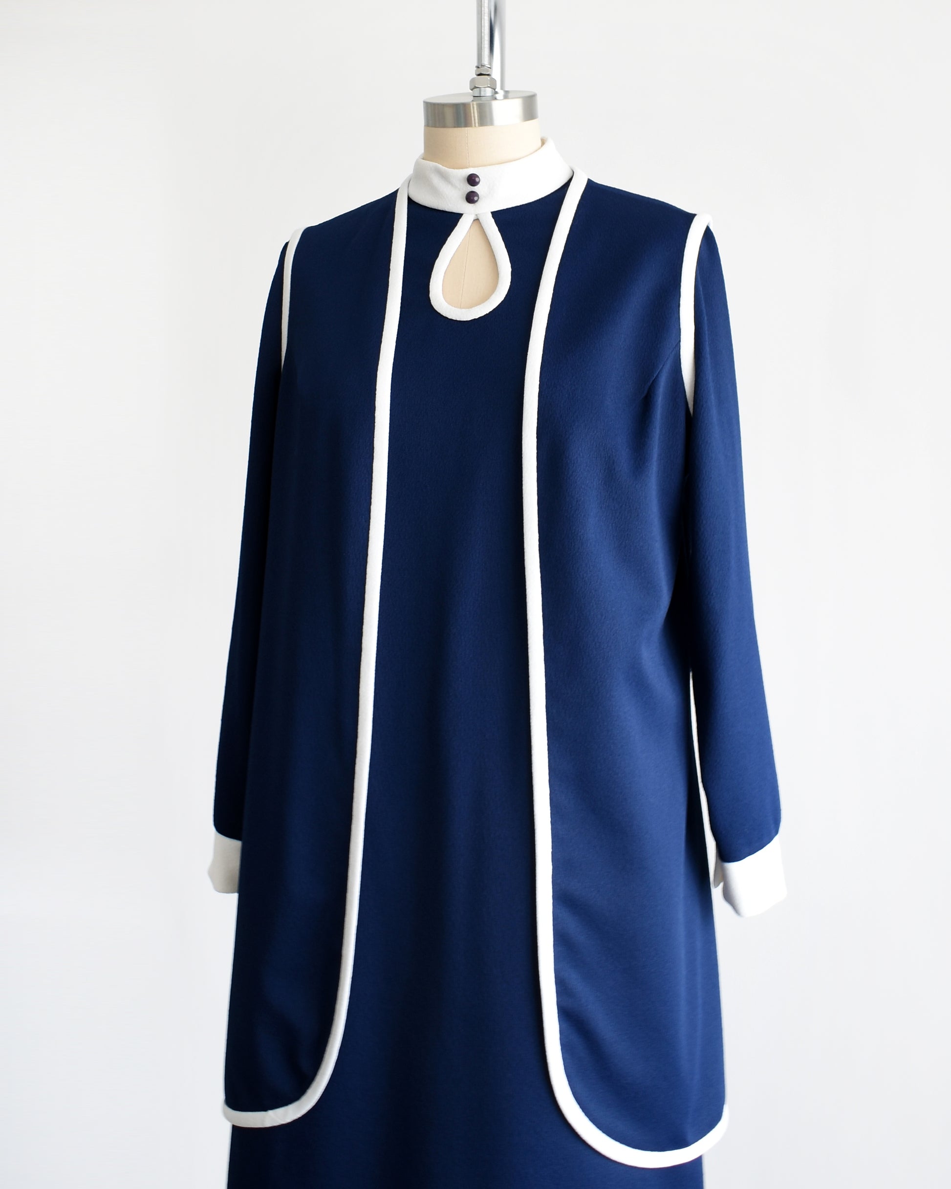 Side front view of a late 1960s to early 1970s mod two piece set features a navy blue long sleeve dress and matching vest 
